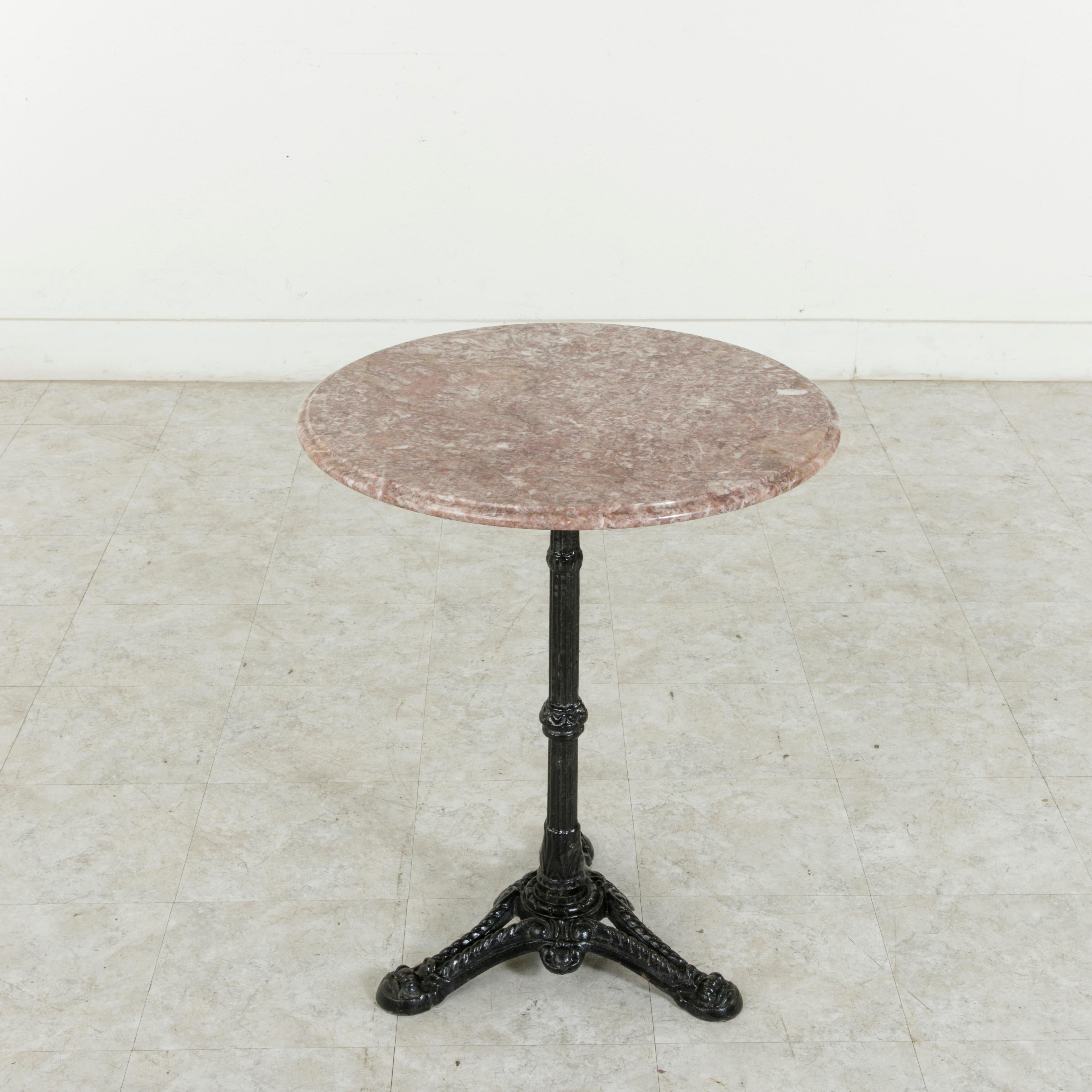This French round bistro table from the turn of the twentieth century features a heavy cast iron tripod base with shell motif. The fluted pedestal stem that supports the bevelled rose marble tabletop is adorned with acanthus leaves. Reminiscent of