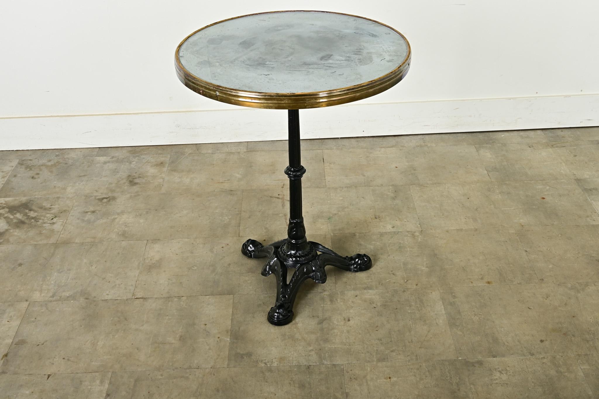 Tavolo da bistrot rotondo in ghisa francese della fine del XIX secolo con piano in acciaio incastonato in una struttura in ottone. La superficie in metallo spazzolato presenta una patina rovinata dal tempo e dall'uso, per essere un punto di appoggio