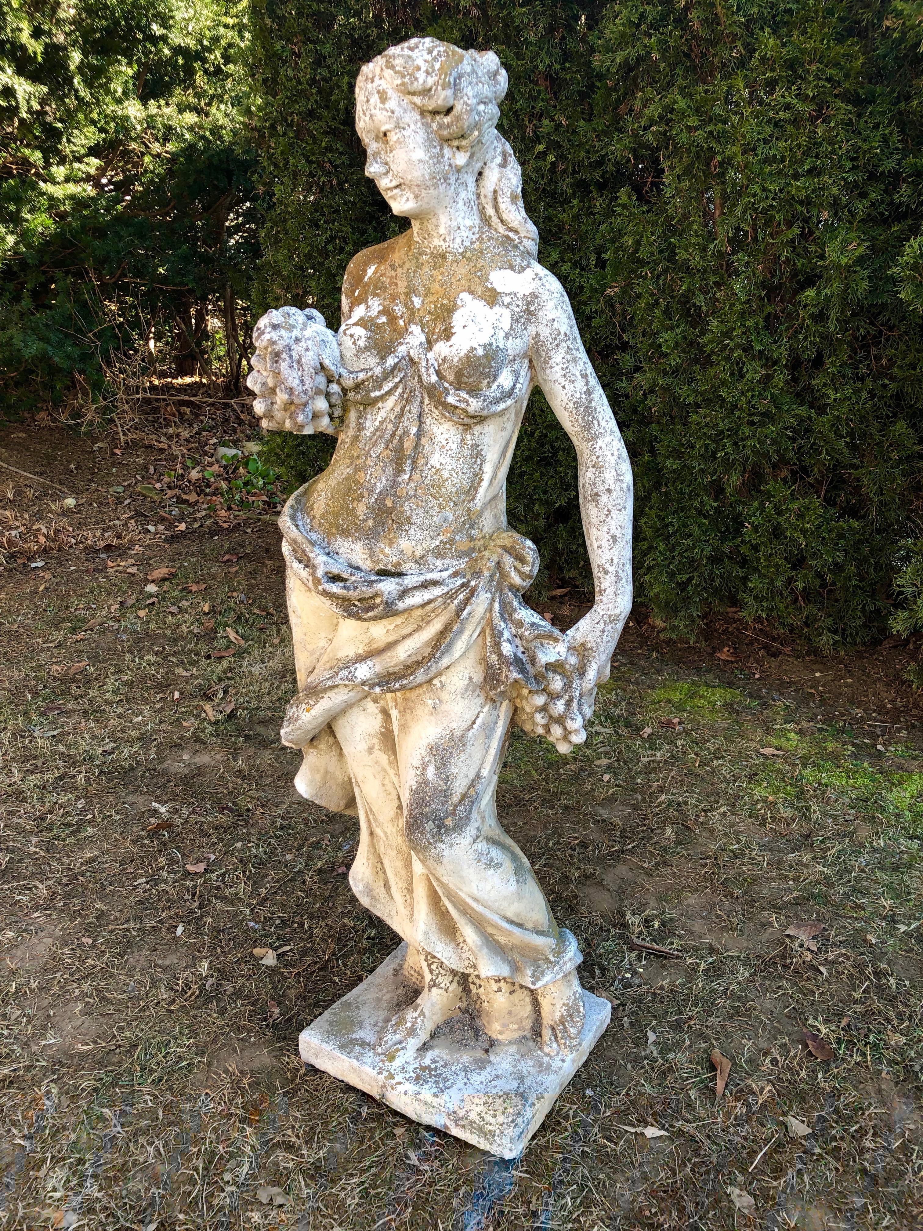 Classical statuary still has a place in the garden or home, and this figure of Autumn is stunning. With a gorgeous weathered patina, heavy yellow lichen, and a small amount of moss, she is posed holding a cluster of grapes across her chest and