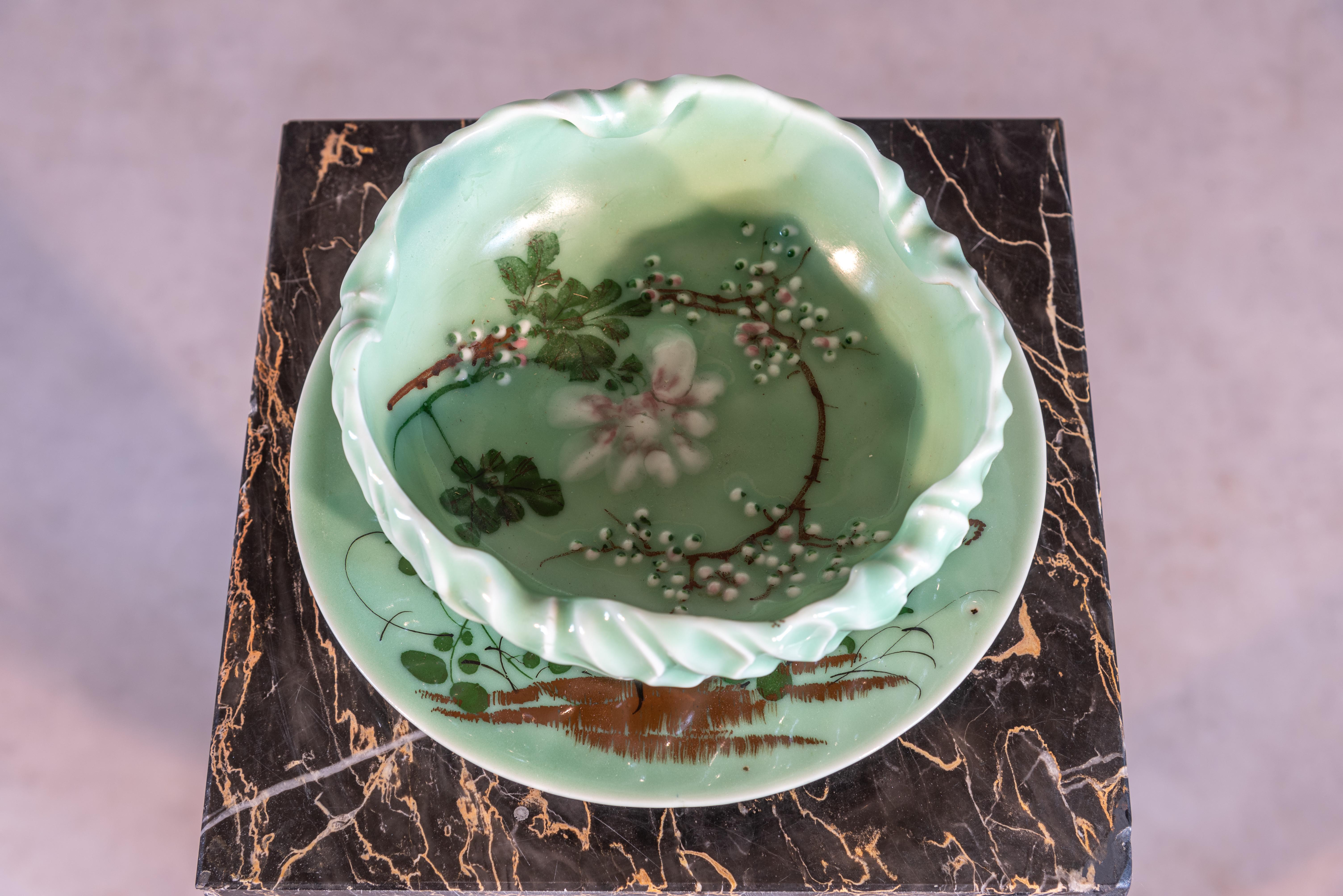 Crafted in the early 20th century, this French Celadon Bowl and Plate duo encapsulates the enduring allure of Art Nouveau aesthetics. The delicate celadon glaze, with its nuanced green tones, serves as a captivating canvas for the intricate flower