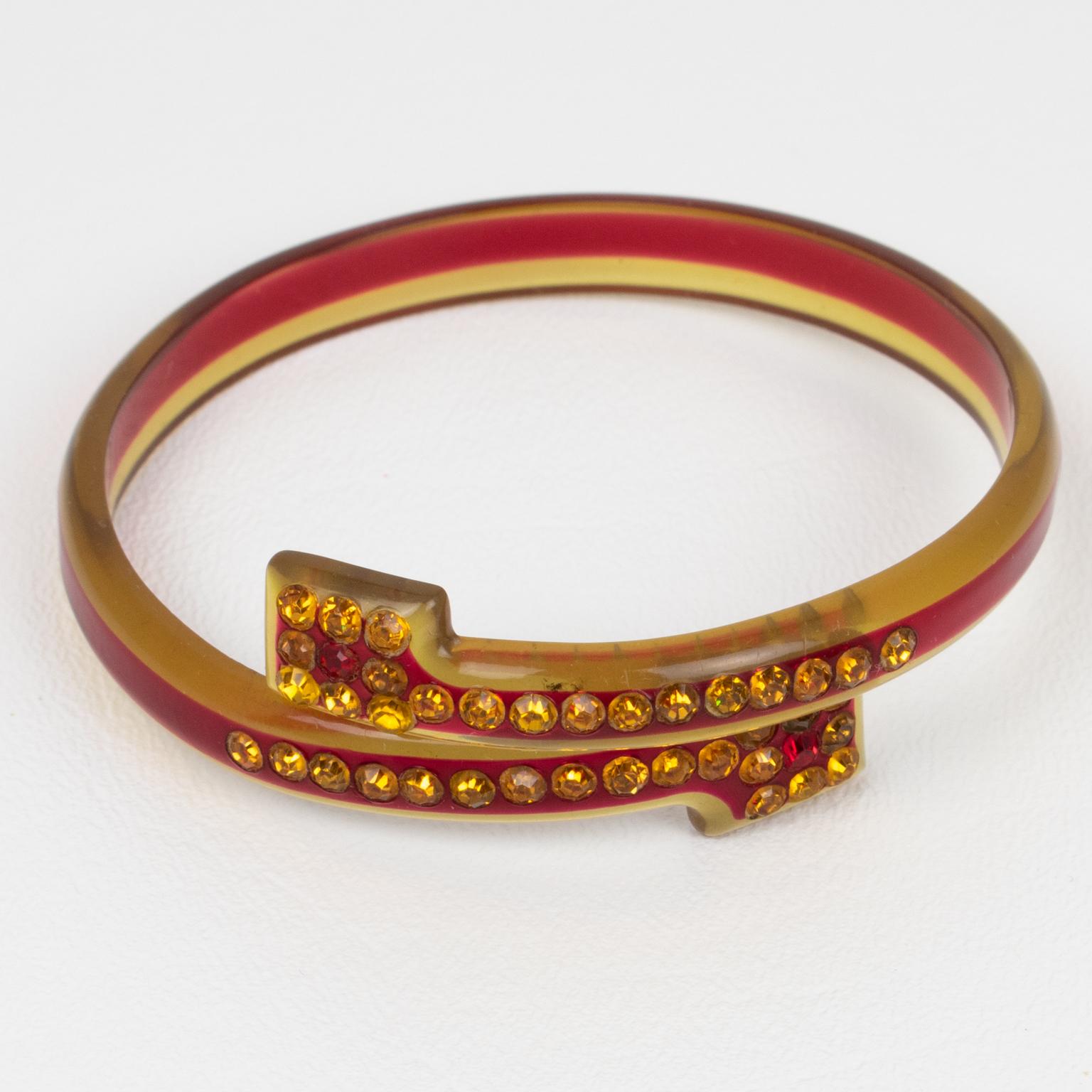 This stunning French celluloid and sparkle bypass bracelet bangle dates from the 1920s. The piece boasts transparent apple juice and red colors with a geometric design and is embellished with orange topaz and ruby-red crystal rhinestones. The 1920s