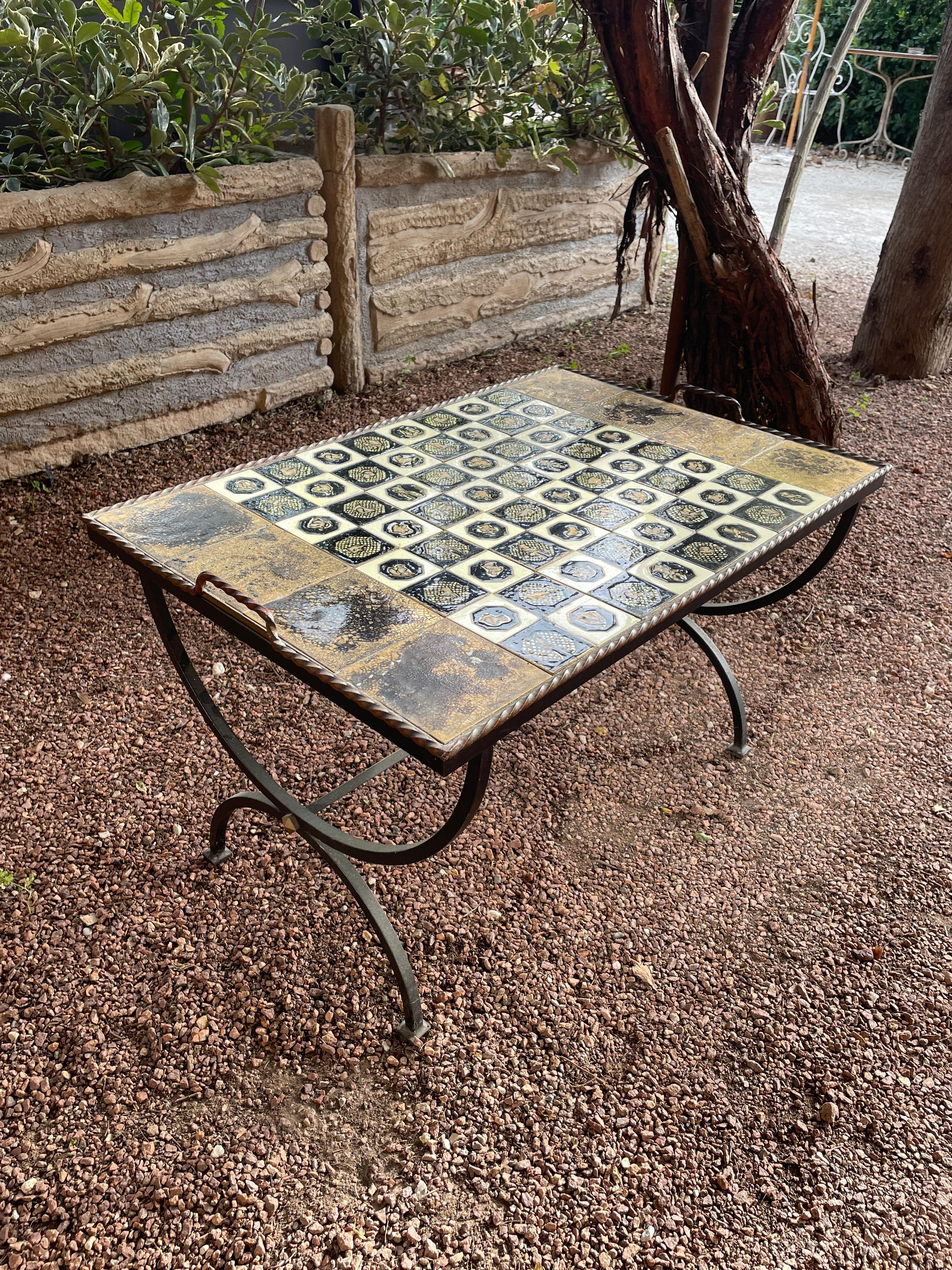 Elegant ceramic coffee table or chess table, crafted in Vallauris, France, in the 1950s.

The piece features a wrought iron frame adorned with a gilded cabochon accent at the intersection of the crossed stretchers, supporting a magnificent glazed
