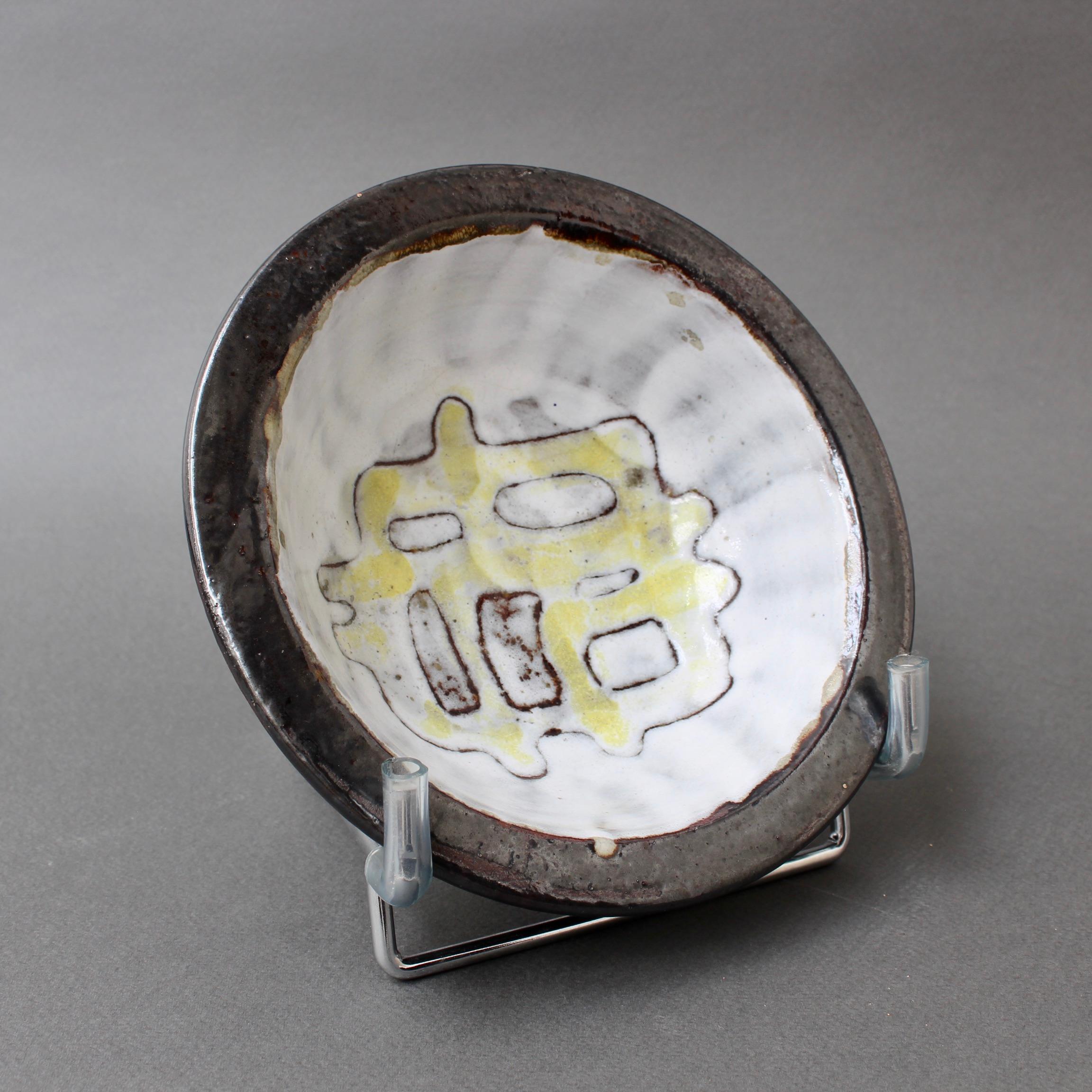 Vintage French ceramic decorative bowl with abstract motif attributed to Jean Rivier (circa 1960s). A small, circular shaped bowl / vide-poche of enamel with a modern linear decoration reminiscent of a labyrinth. The subtle yellow backdrop colour