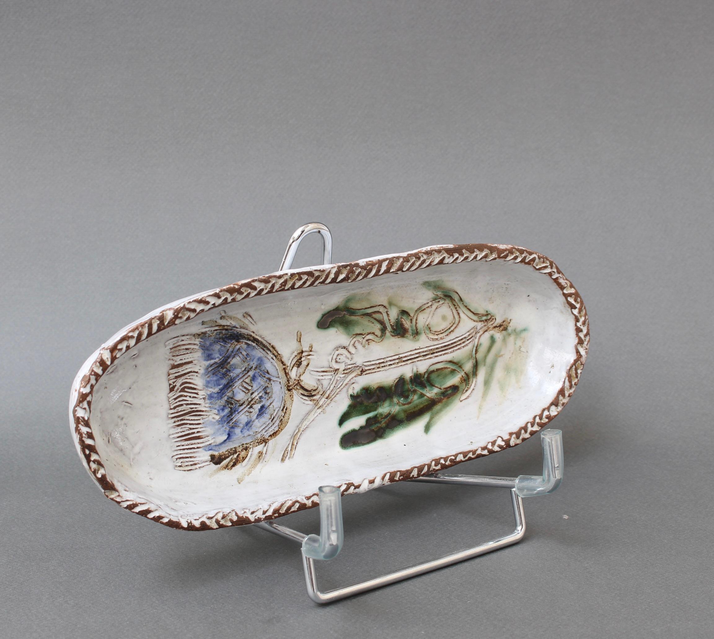 French ceramic decorative dish with flower motif (circa 1970s) by Albert Thiry. An oblong-shaped ceramic dish has a chalk-white glaze surface. Within the dish's recess, a thistle flower is incised into the glaze and painted in Thiry's trademark