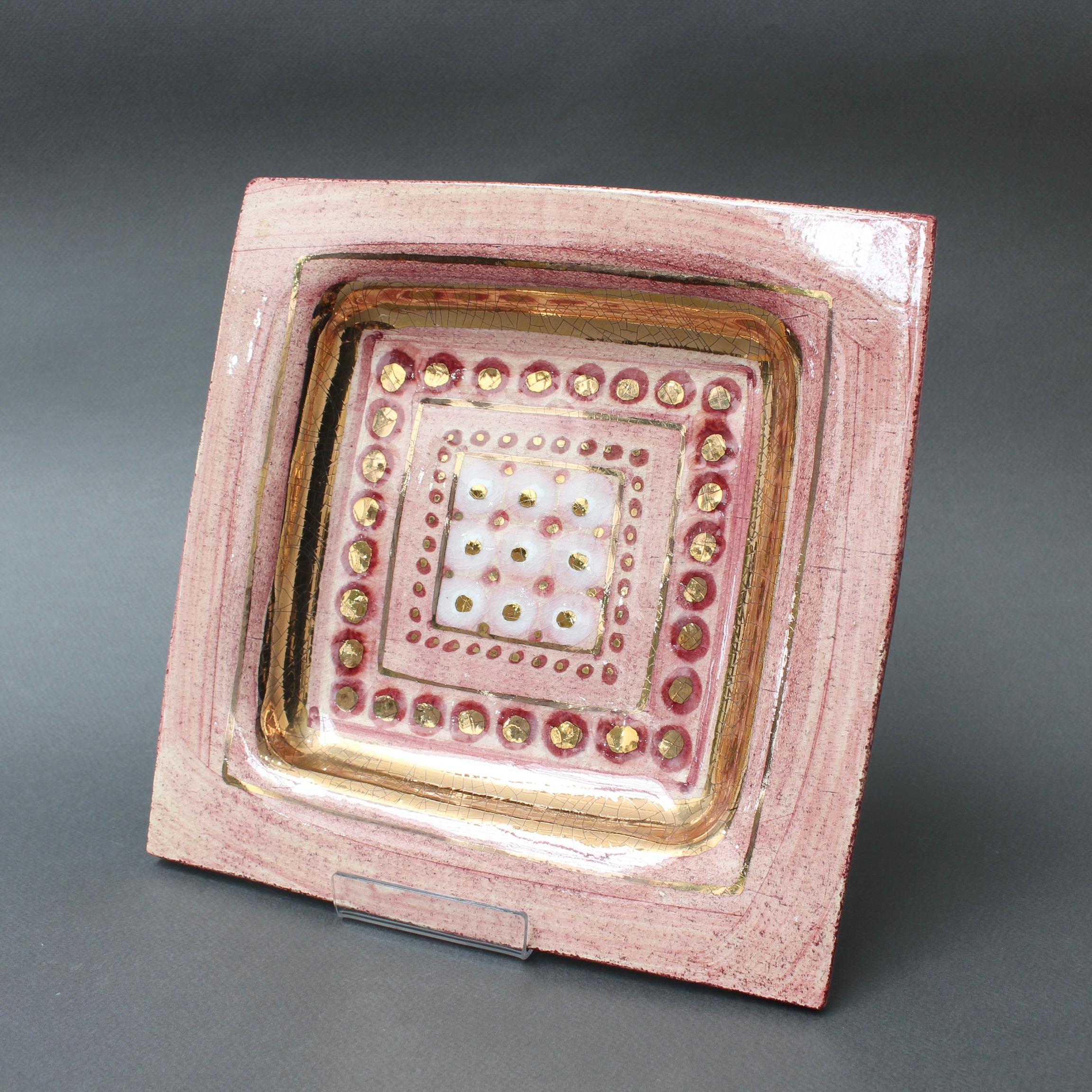 French pink decorative plate by ceramicist Georges Pelletier, (circa 1970s). Handmade, ceramic with crimson trim and gold-lustre craquelure. The sunken base of the square presents a series of gold geometric shapes in a repeating square pattern. The