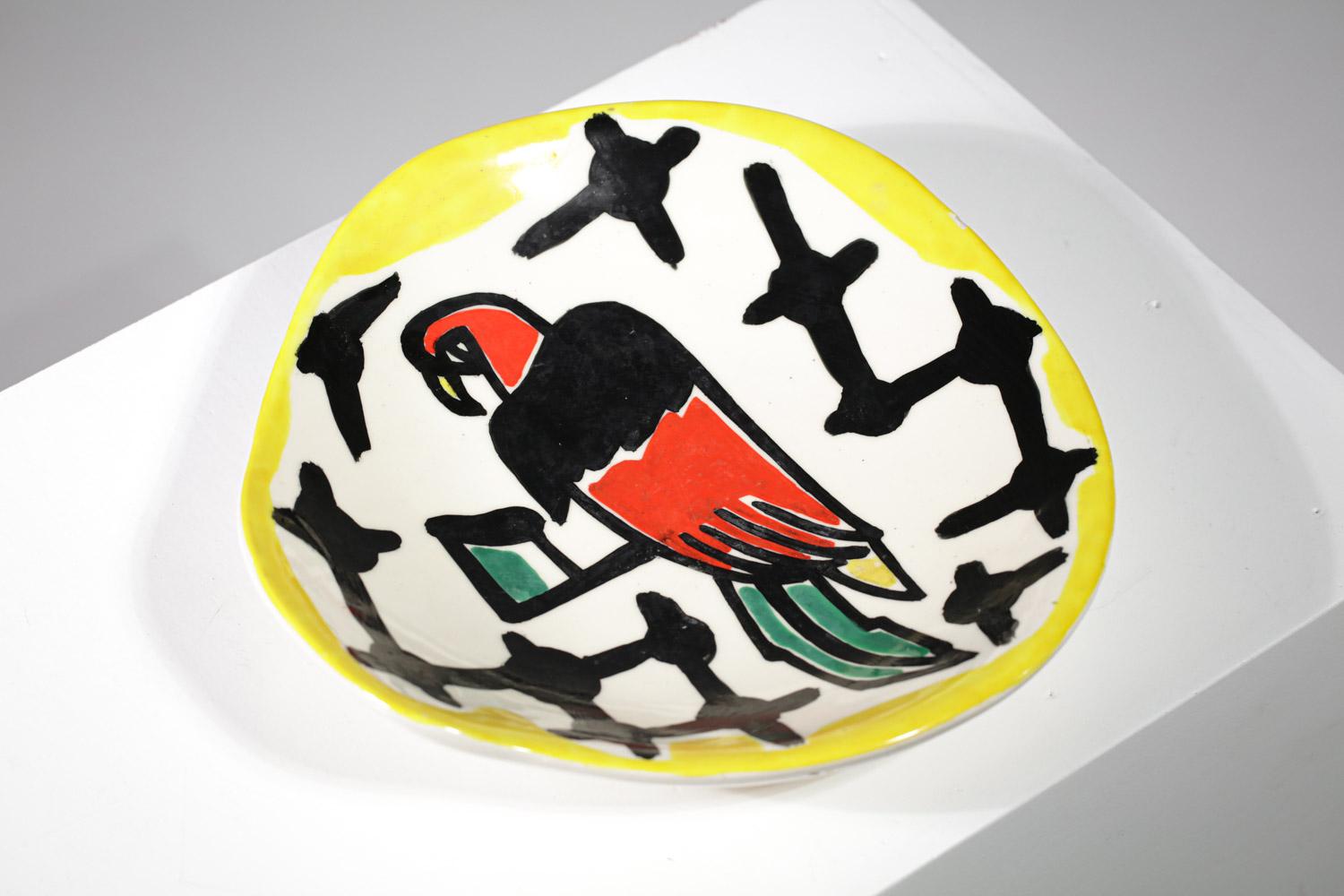 Plat ou tasse des années 50 du céramiste français Roland Brice provenant des ateliers de Biot. Bol de forme libre en faïence blanche avec un décor peint représentant un perroquet dans des couleurs vives typiques de l'artiste et du style de Fernand