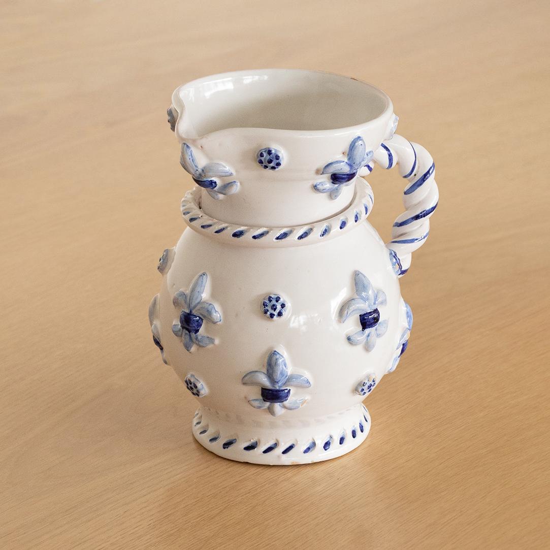 Beautiful ceramic pitcher from France, 1950's.  White glossy pitcher with twisted ceramic handle and ornate ceramic appliques painted in a beautiful blue accent color. Unique and eye catching piece. 
   