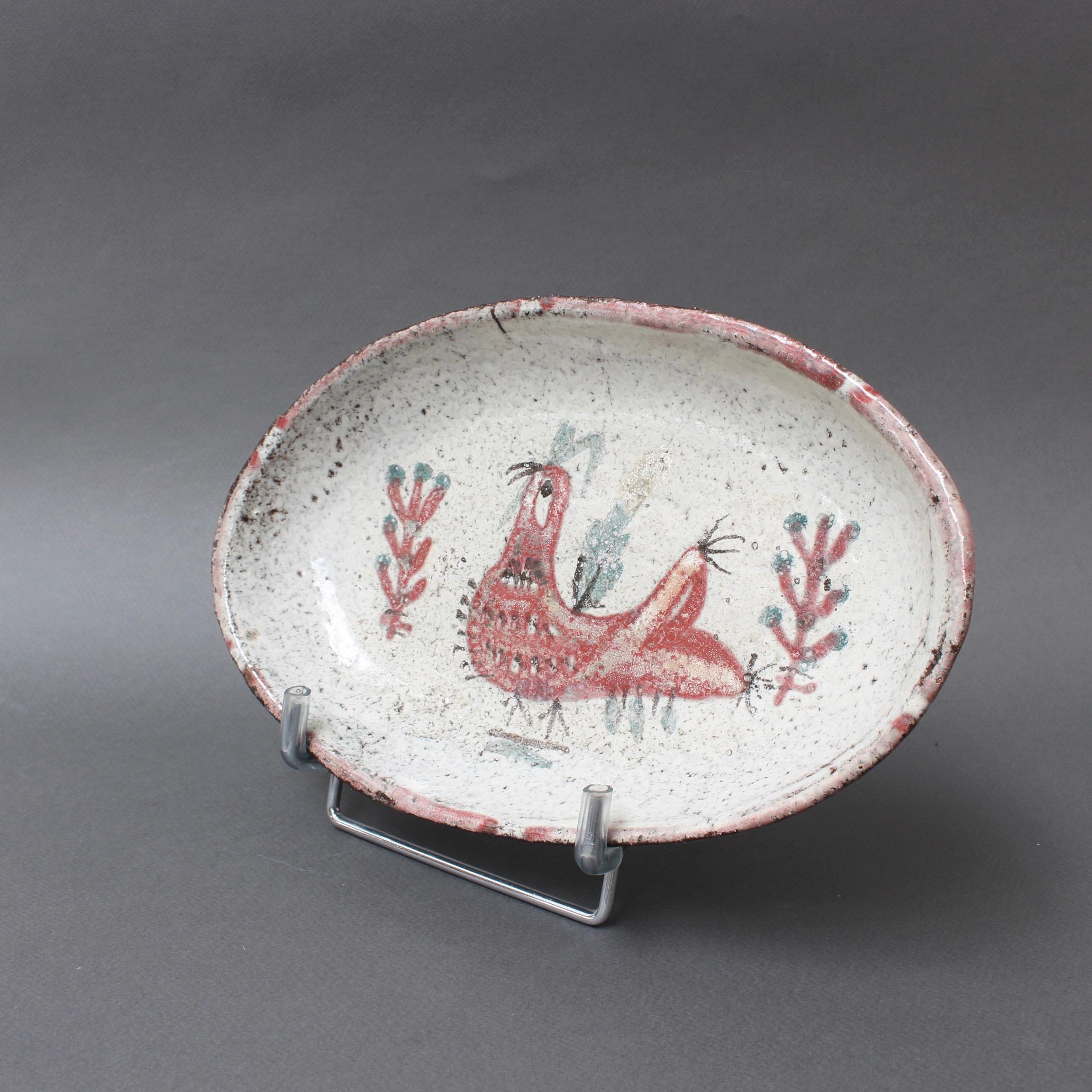 French ceramic Rooster motif tray by Gustave Reynaud (circa 1950s). Oval-shaped tray with raised rim in earthenware presenting decor of a French rooster and stylised foliage. The rooster is mulberry red and on its side are mulberry and green