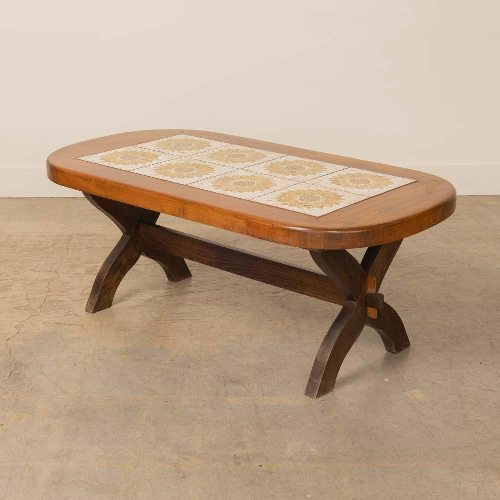 Lovely ceramic tile and wood coffee table from France, 1960s. Rectangular table top with rounded corners on a carved x base. Beautiful ceramic tiles with painted floral design in yellow, cream, and brown. Original finish shows nice age and patina. 