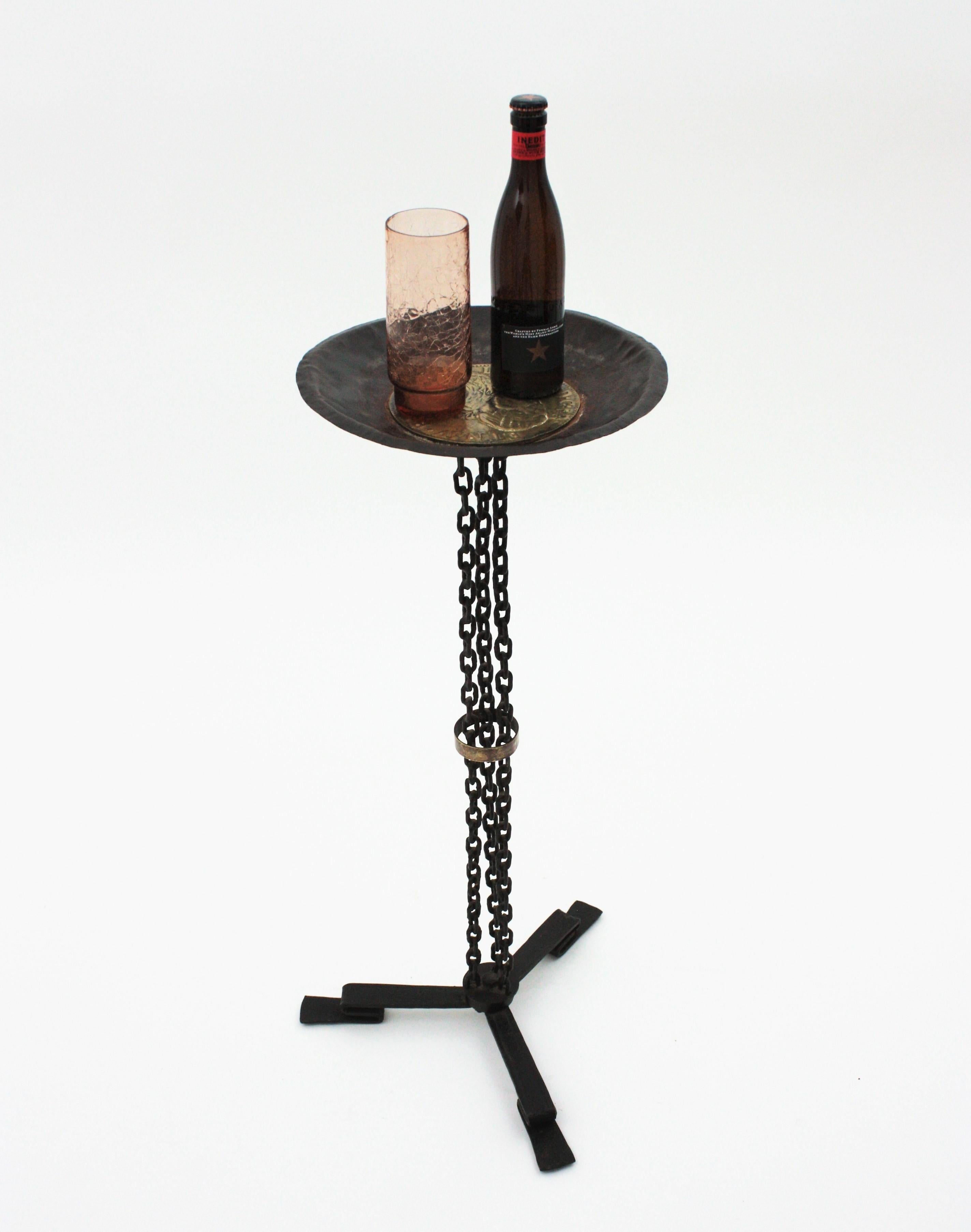 Chain Link End Table or Stand in hand forged iron with brass coin decorative panel. France, 1930s
This colonial revival pedestal table or stand features a base with 3 iron chains standing on tripod feet. The top is adorned by a brass large Louis