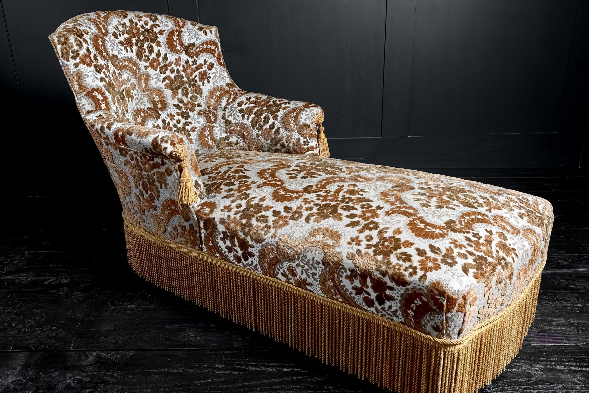 Méridienne à chaise longue de style second empire du début du 20ème siècle. Accoudoirs à volutes avec glands en soie et jupe frangée assortie, tapisserie en brocart immaculée. Vers 1910.