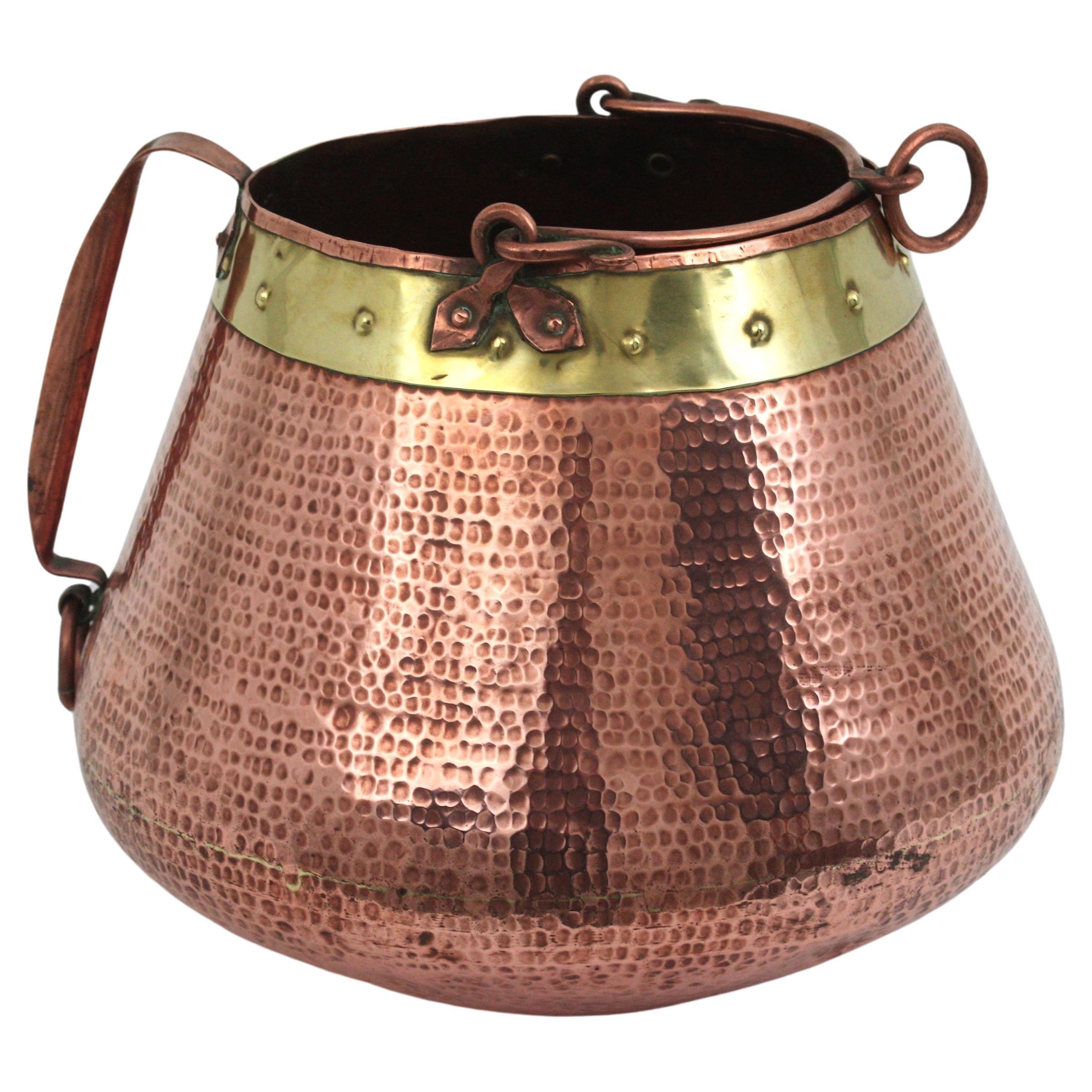 French copper and brass ice bucket or wine / champagne cooler with single handle
This hand-hammered copper cauldron is heavily adorned by the hammer marks thorough and a brass ring with studs on the top.  It has a copper foldable handle with a ring