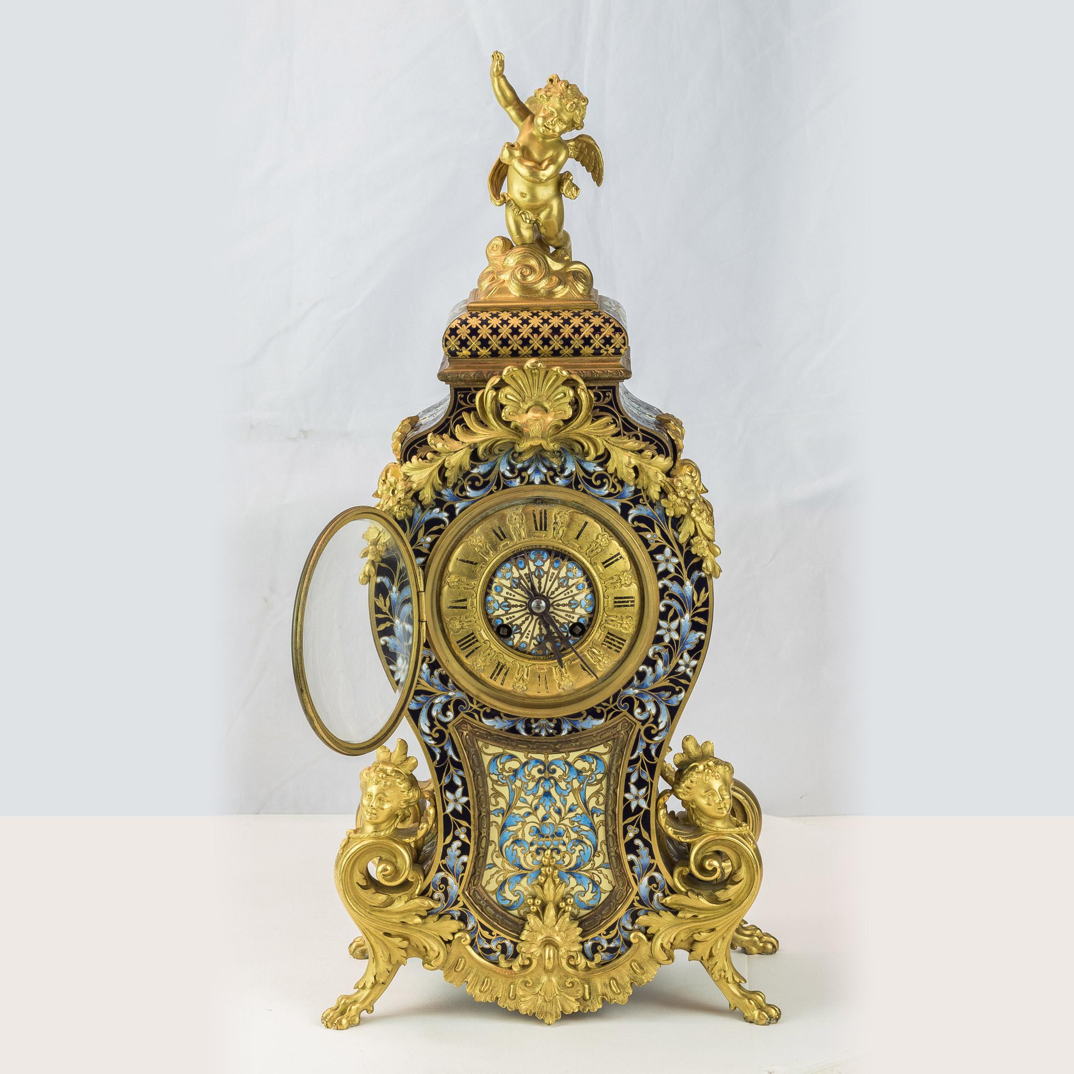 Ormolu and champlevé undulating figural mantel clock surmounted by a gilt cupid in the waves. Ormolu shell and floral mounts above and a plaque below with the base embellished with scrolled gilt god heads and acanthus leaf ormolu all sitting on