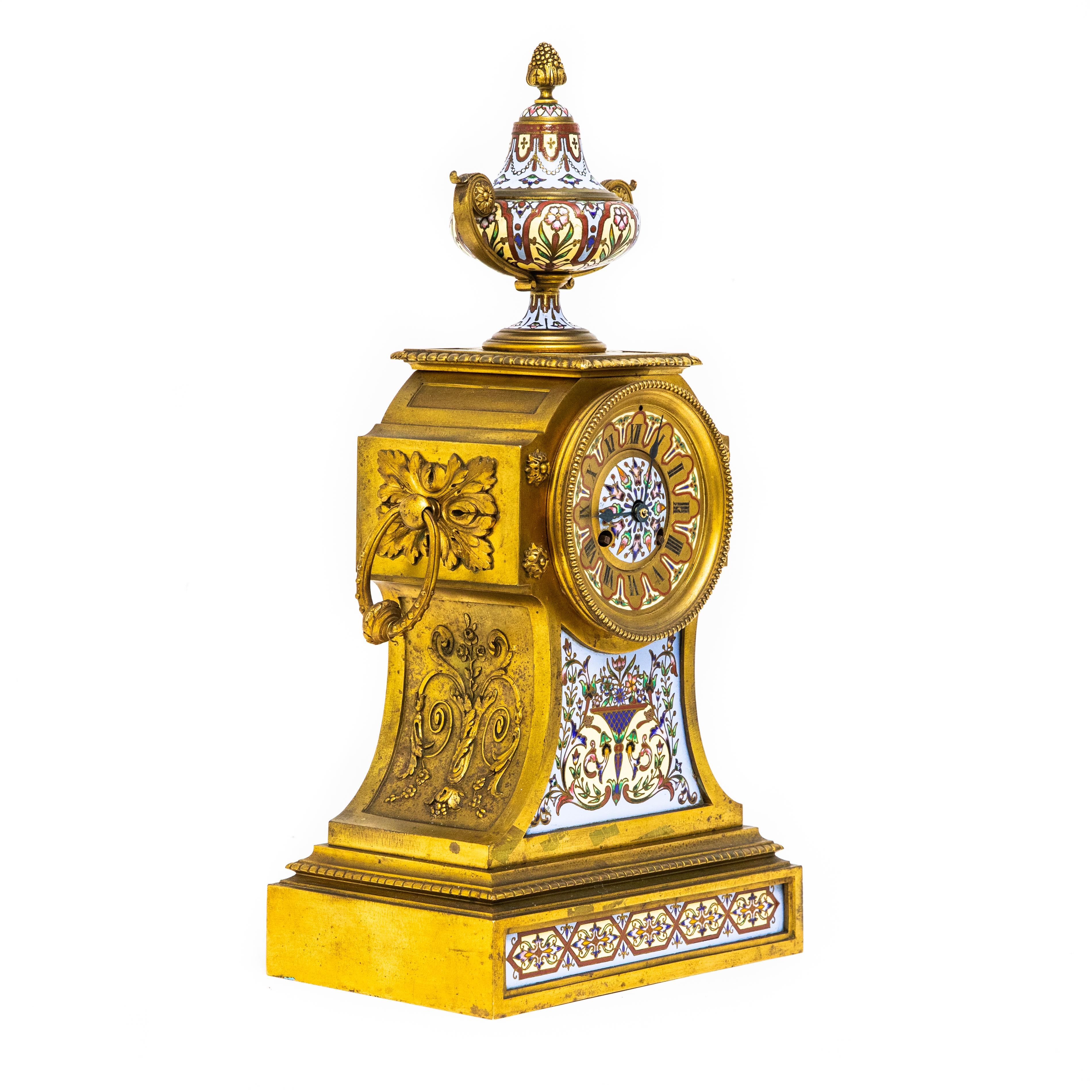Offered is a French champlevé enamel gilt bronze mantel clock with roman numerals, surmounted by an urn finial. Measures: 18.5