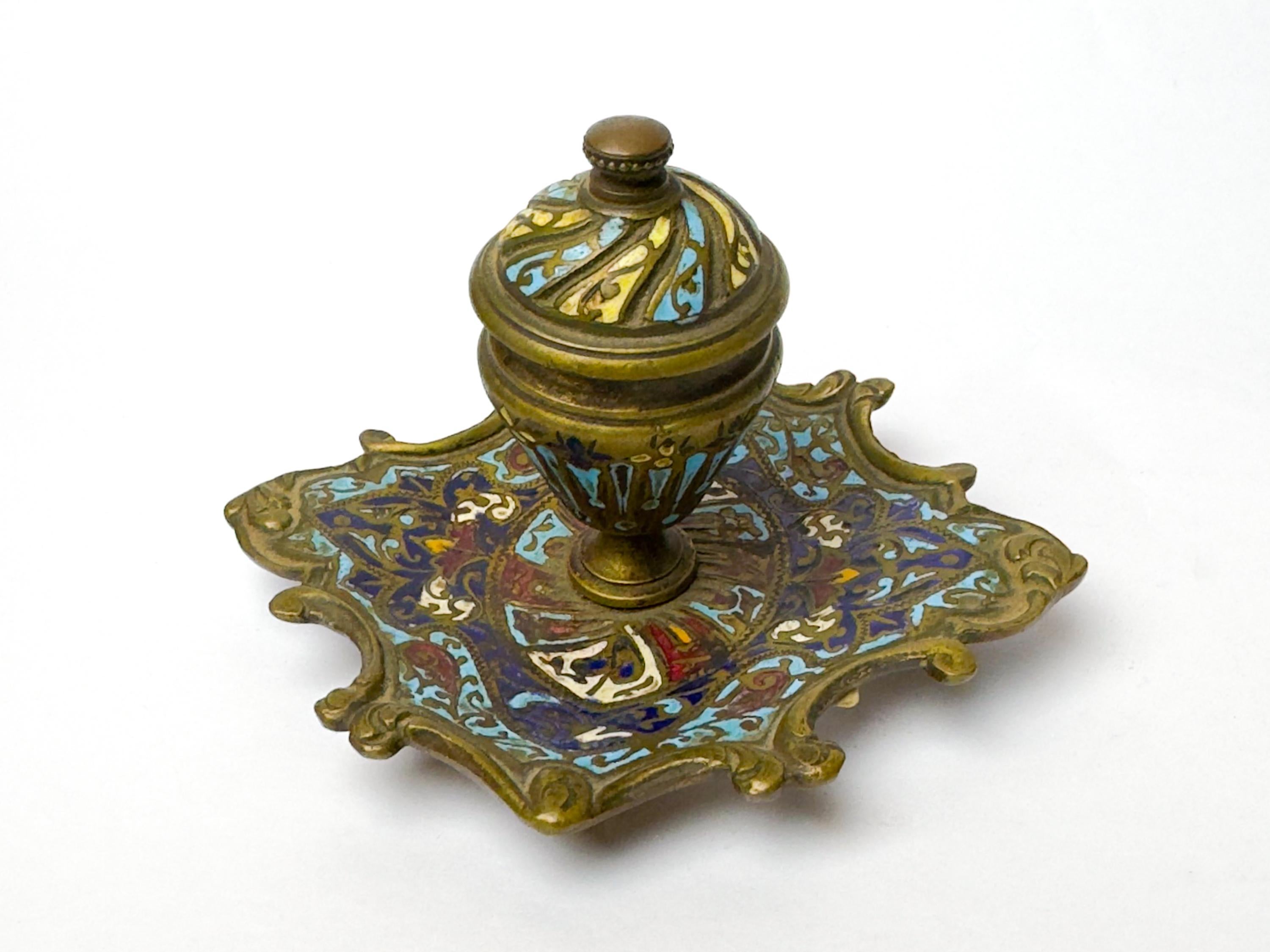 Ein französisches Champlevé-Email-Tintenfass aus dem 19. Jahrhundert, das im opulenten Stil Napoleons III. geschaffen wurde. 

Das Tintenfass ist aus vergoldeter Bronze mit feiner polychromer Emaille in Türkis-, Tiefblau-, Rot-, Gelb- und Goldtönen