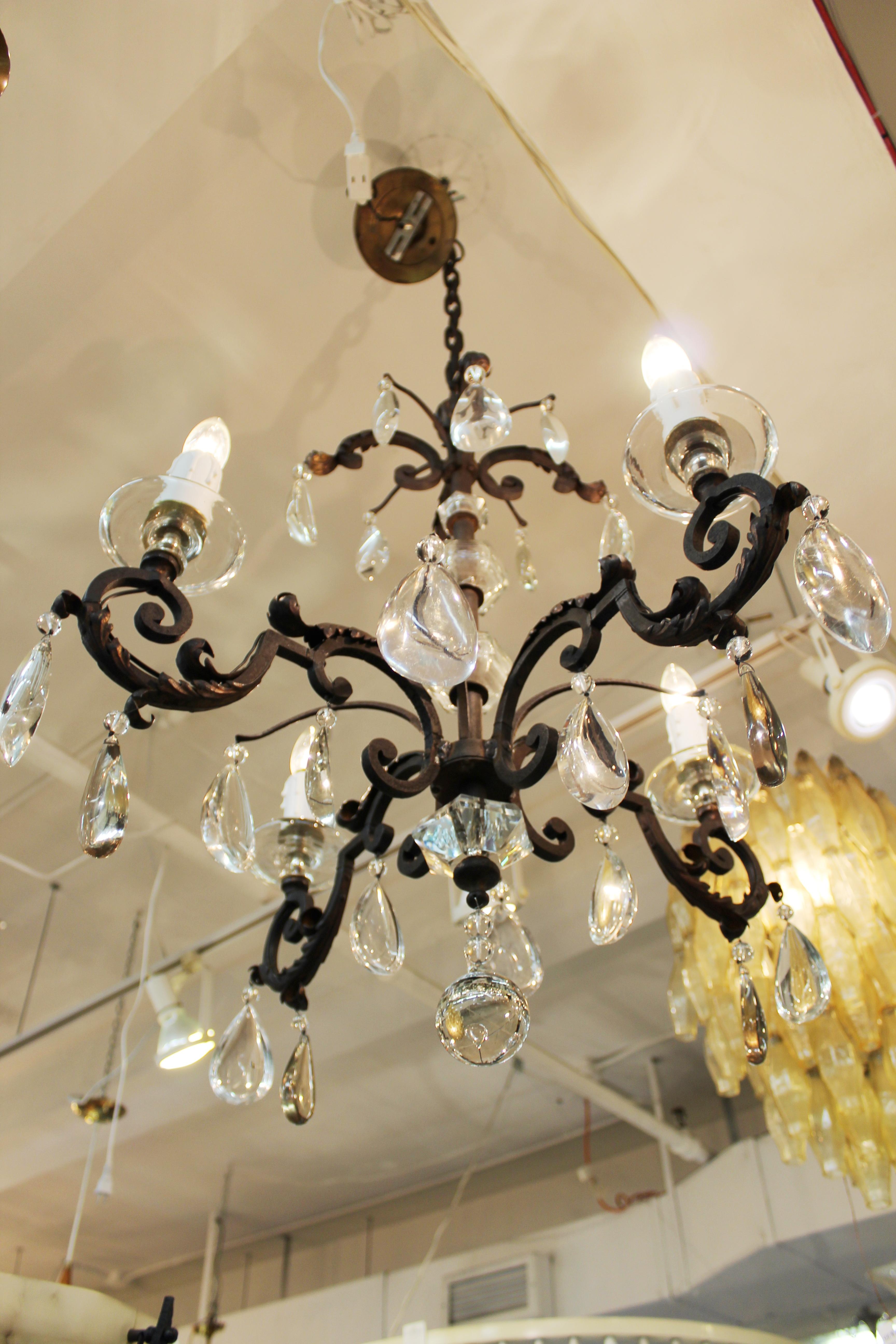 French chandelier dating from the 1940s in patinated metal. Features include four intricately scrolled arms with thick faux candle sockets atop cut crystal bobeches. Large crystal droplets dangle from each limb of the chandelier. Despite wear
