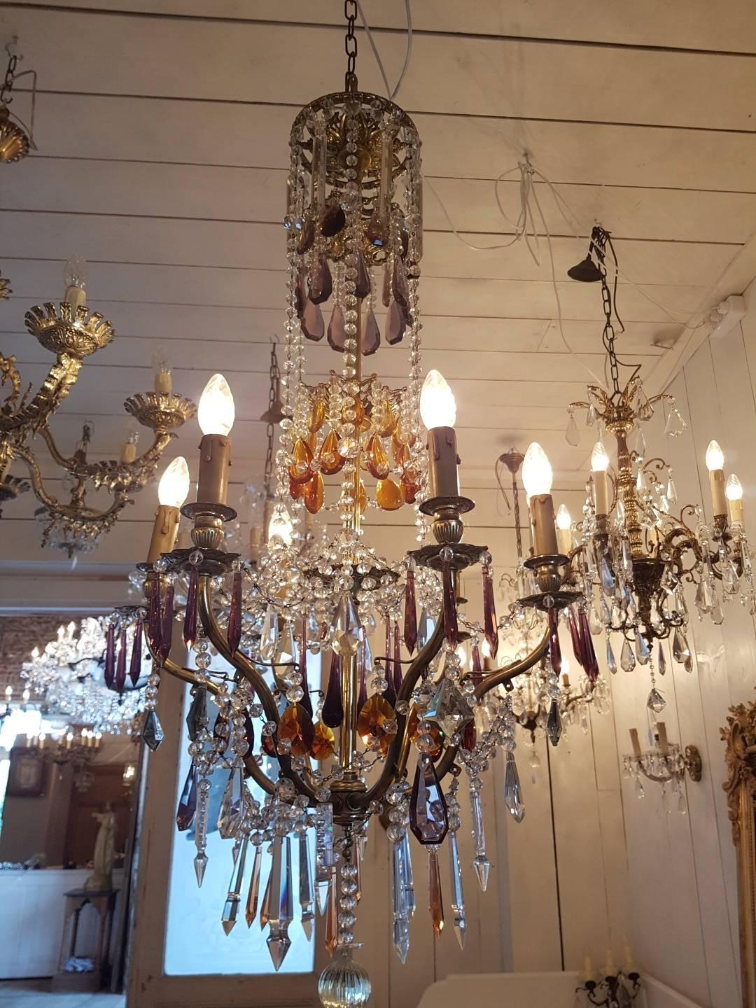 Unique French chandelier with six candle lights, decorated with clear crystals and colored pieces like purple and amber. The chandelier is tall with a diameter of 55 cm and a length of 110 cm without chain.