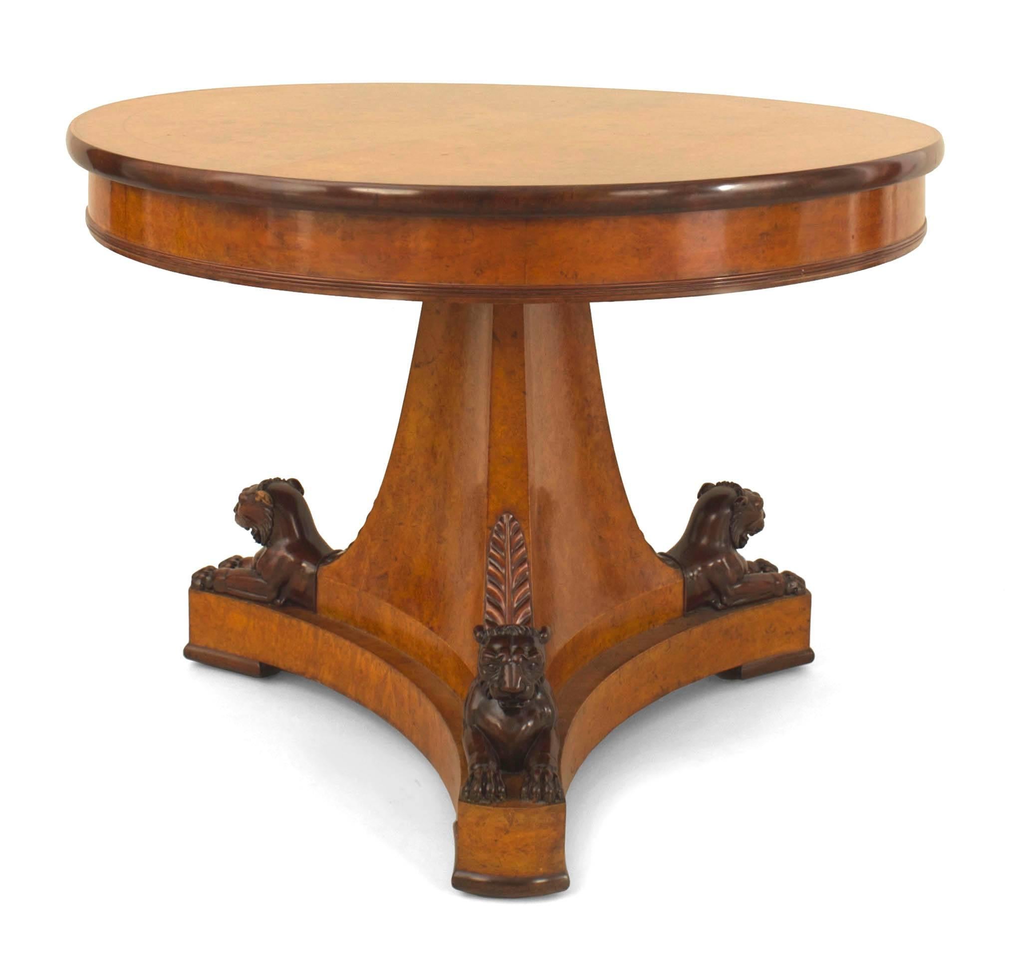 French Charles X (1830s) amaranth wood center table with a banded inlaid round top resting on a triangular pedestal base with mahogany carved trim and reclining lions.
