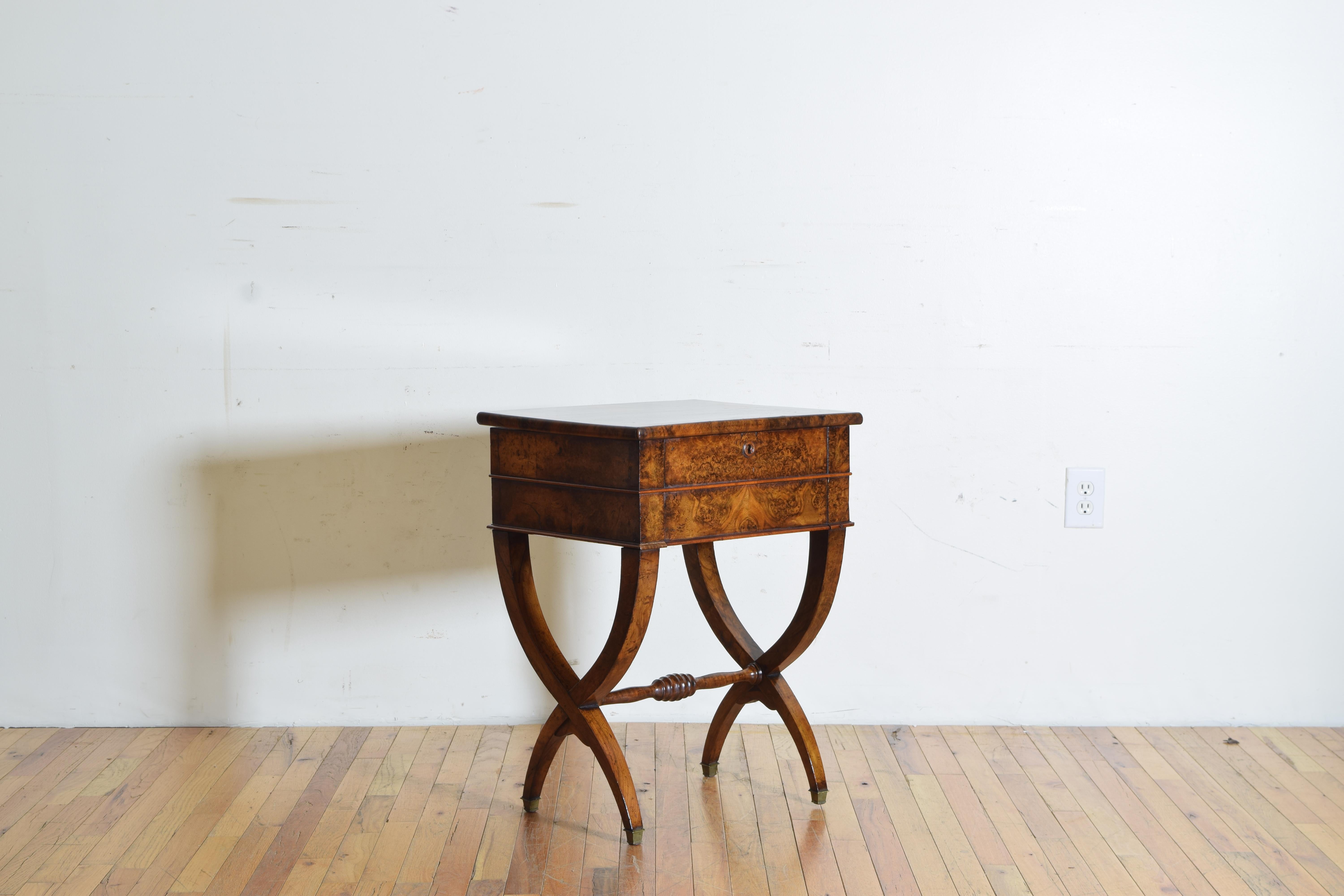 Having a hinged square top opening to reveal a storage well and a mirrored surface with an additional lower drawer, raised on curule form legs joined by a turned stretcher, the feet with brass casters.