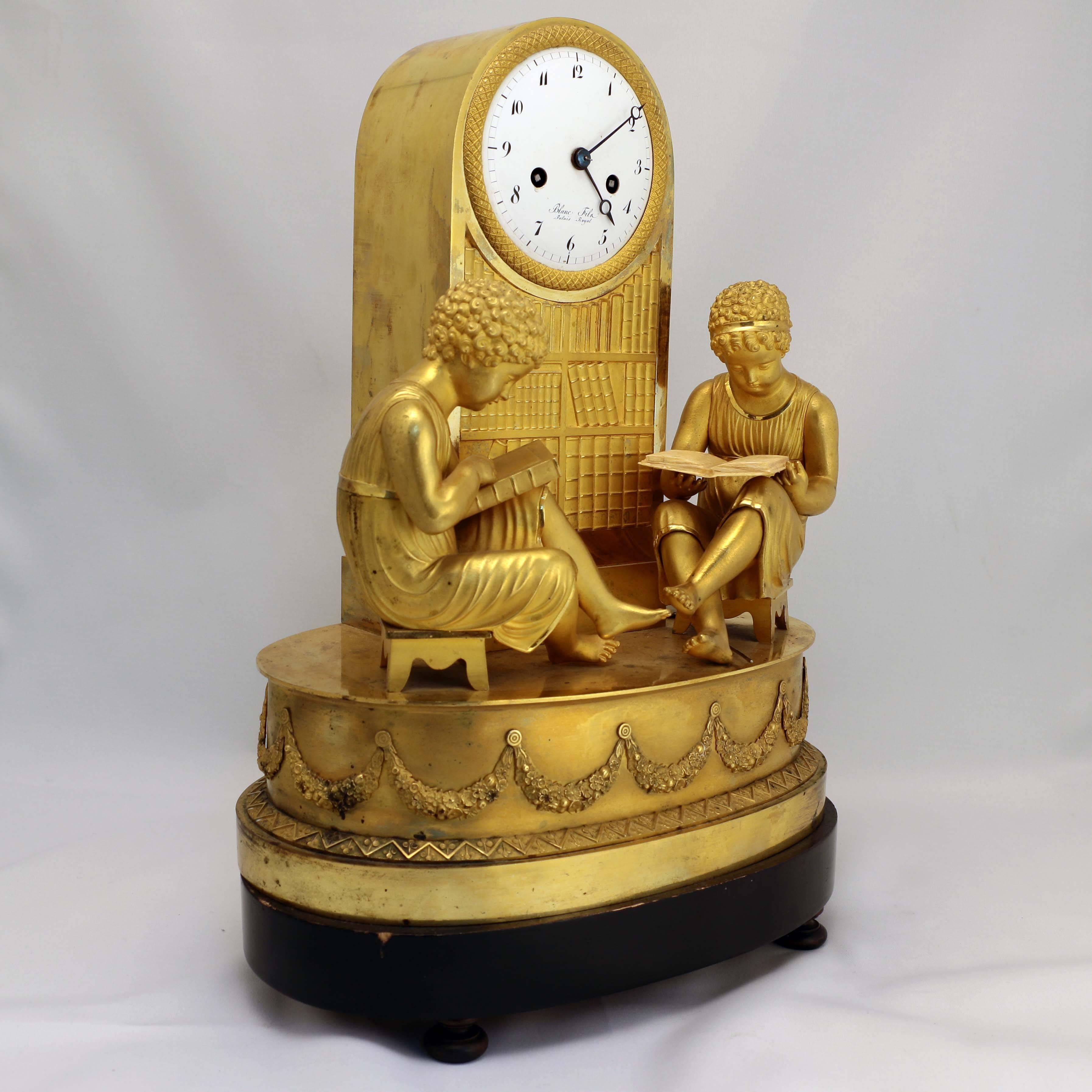 This unusual clock signed Blanc Fils Palais Royal is modelled as a library, flanked by two seated children engrossed in books with a bookcase in the background. It is crisply modelled and of a fine warm color, with enamelled dial and blued steel