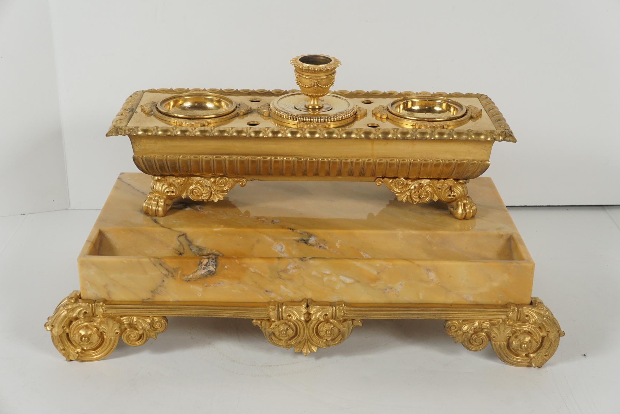 This French carved marble and gilded bronze inkwell and candlestand, circa 1830 is carved from sienna marble. The large block is set with a tray well in front and then the cast bronze sarcophagus shaped inkwell is set up on animal paw feet. Cast