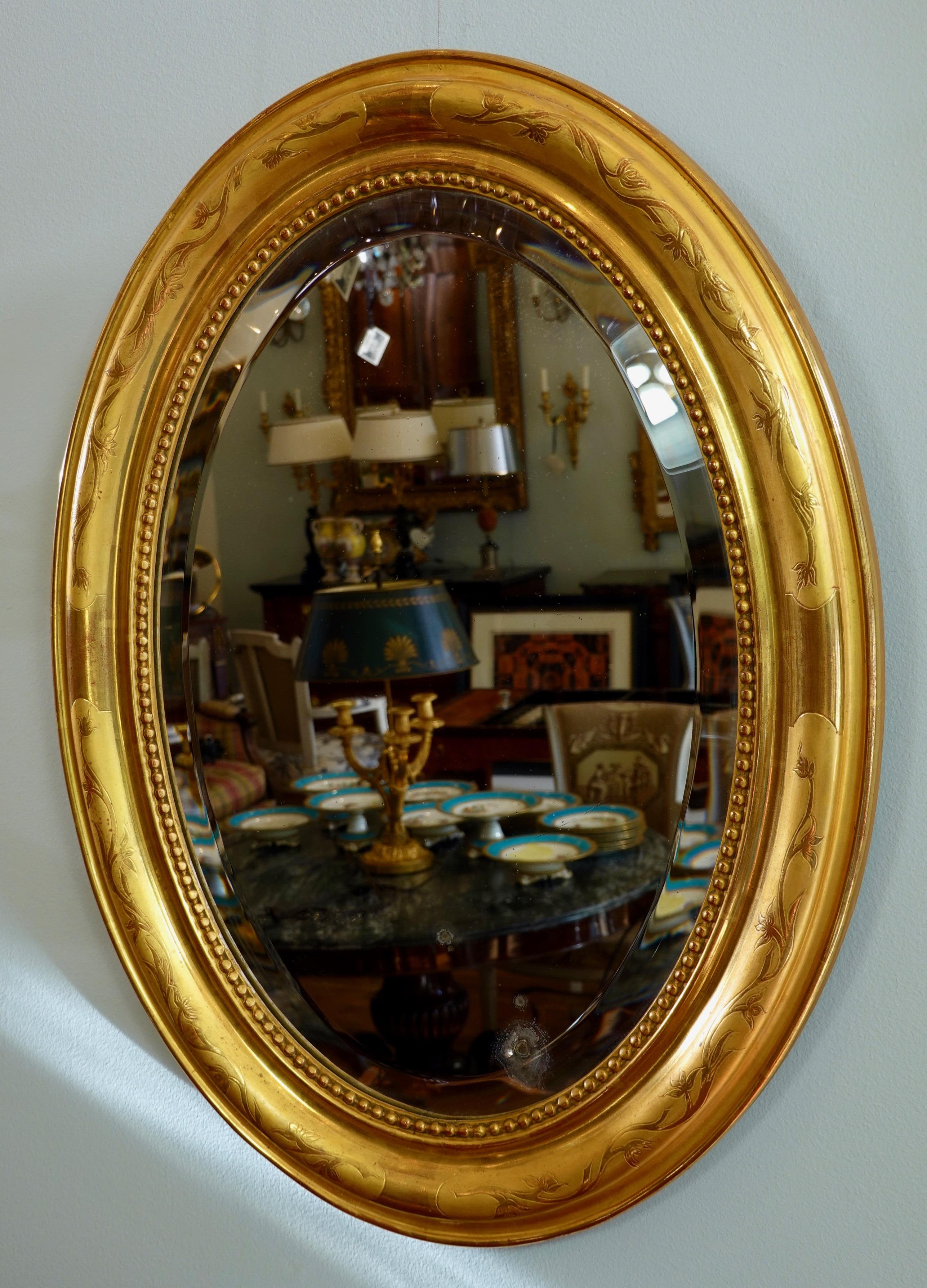 Ovaler französischer Spiegel Charles X mit originalem, abgeschrägtem Glas. Der Rahmen ist tief ausgeformt mit einem Rankenmuster und Perlenketten um den Innenumfang. Das Glas ist leicht beschädigt.