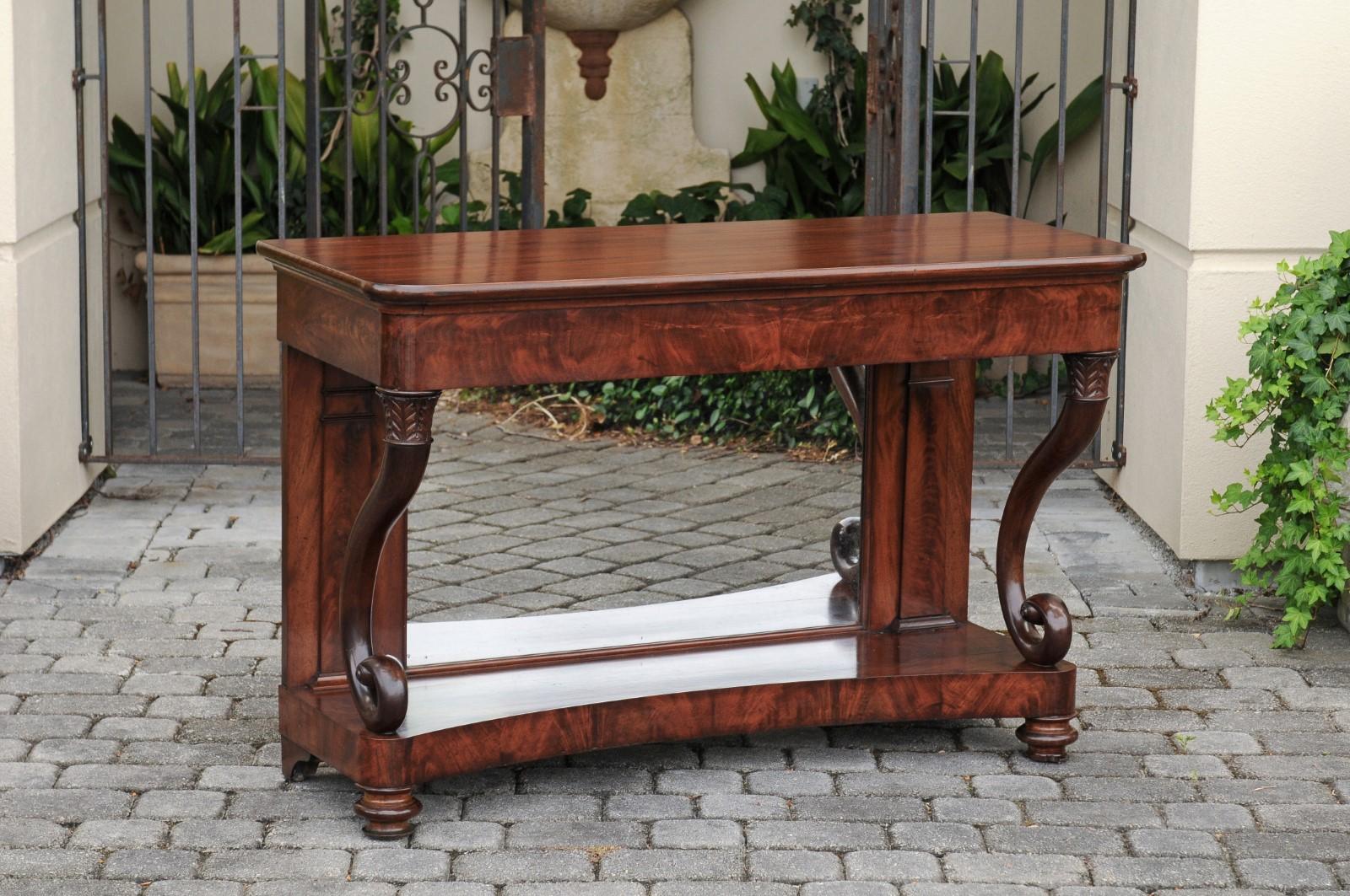 A French Charles X period mahogany console table from the 19th century, with cornucopia legs, lower shelf and mirror. Born in France during the first half of the 19th century, this exquisite mahogany console table features a rectangular top with