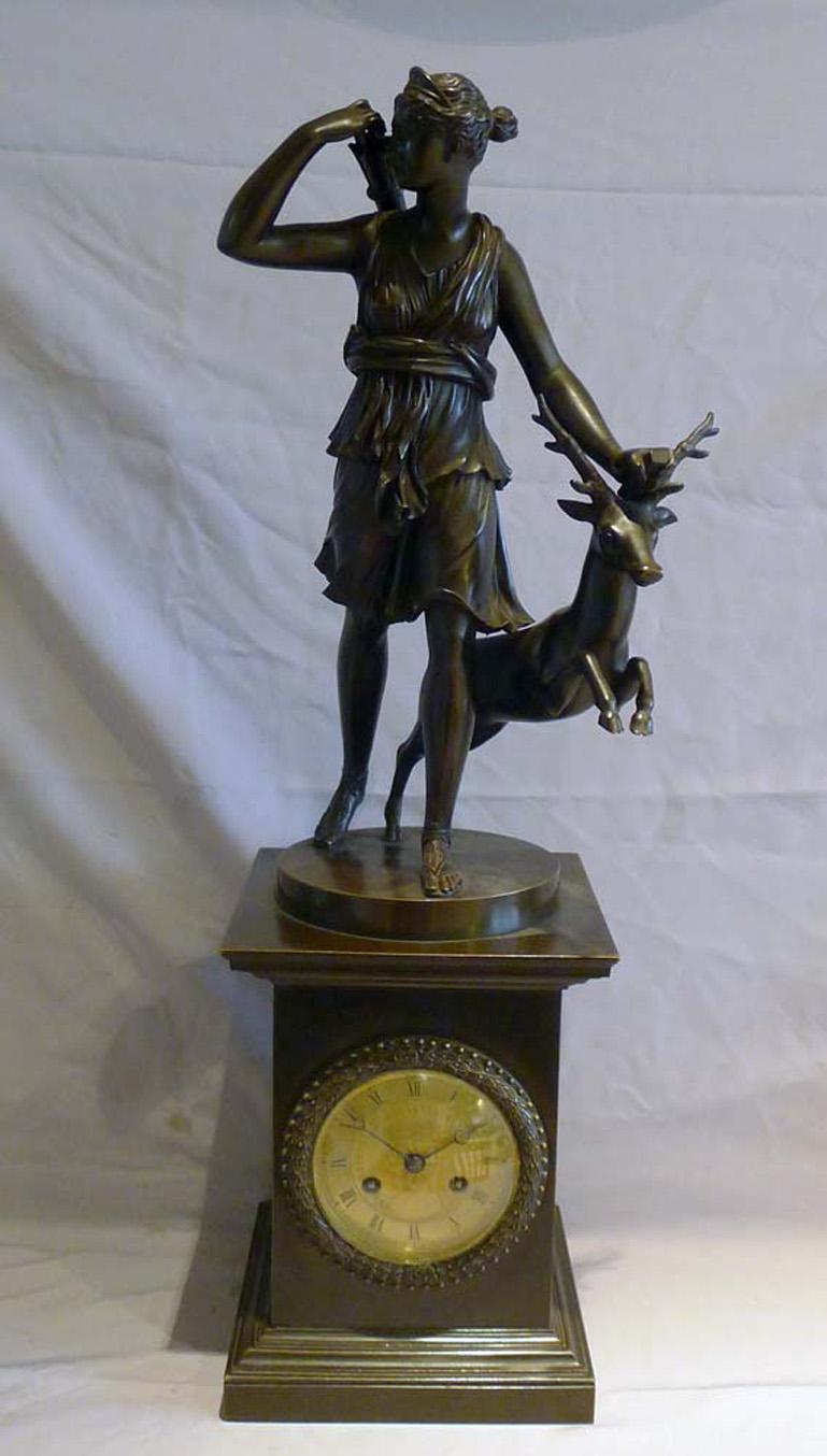 French Charles X period patinated bronze mantel clock with bronze of Diana and deer. Set upon a square base with mouldings top and bottom and the clock face set centrally. The fine bronze of Diana the Huntress, after the antique stands on a circular