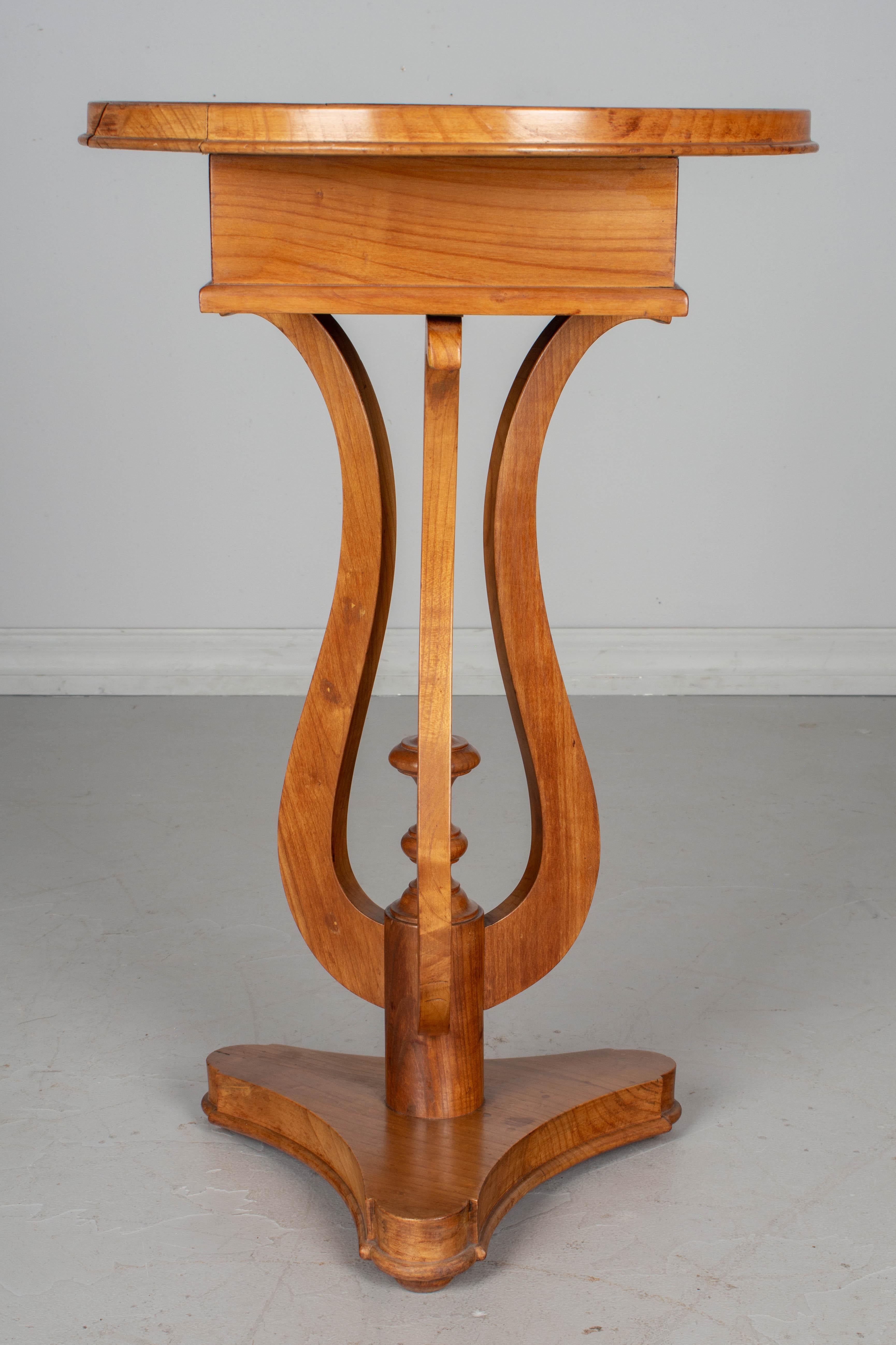 A French Charles X style gueridon made of solid cherrywood. A nice circular accent table with lyre shaped pedestal, turned finial and triangular base. Small dovetailed drawer with brass knob. Please refer to photos for more details.
  
