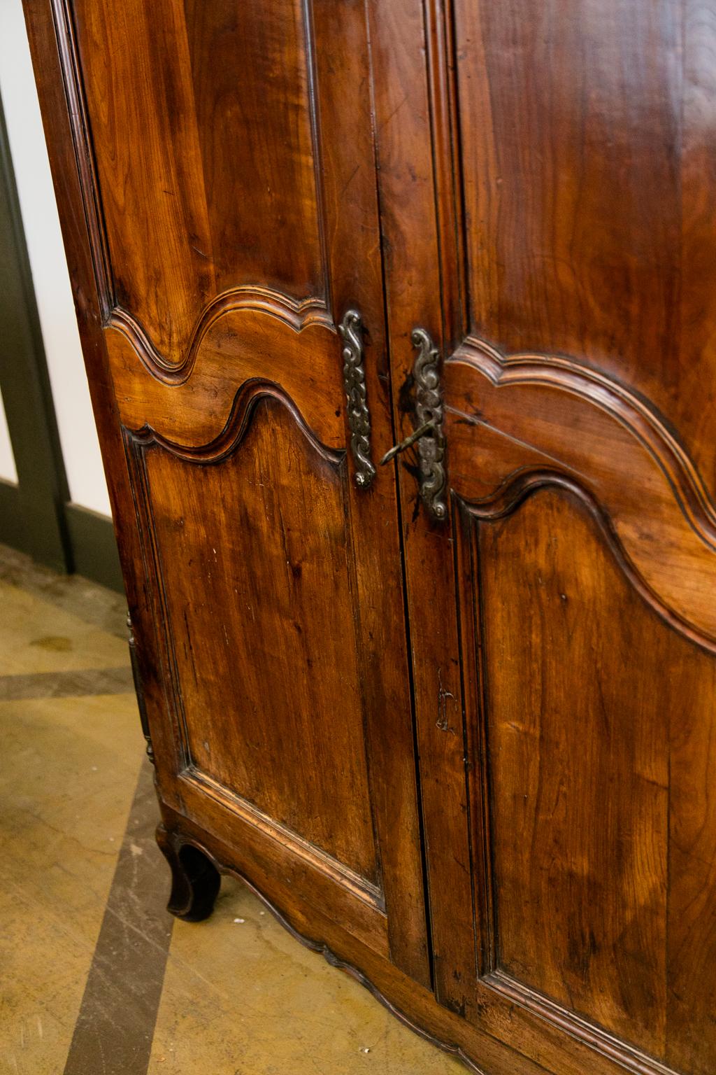 French cherry armoire has the original steel hardware and working lock and key. The front and cornice are made of cherry. The front has a recessed paneled frieze and a removable cherry cornice. The doors are on removable hinges and have shaped
