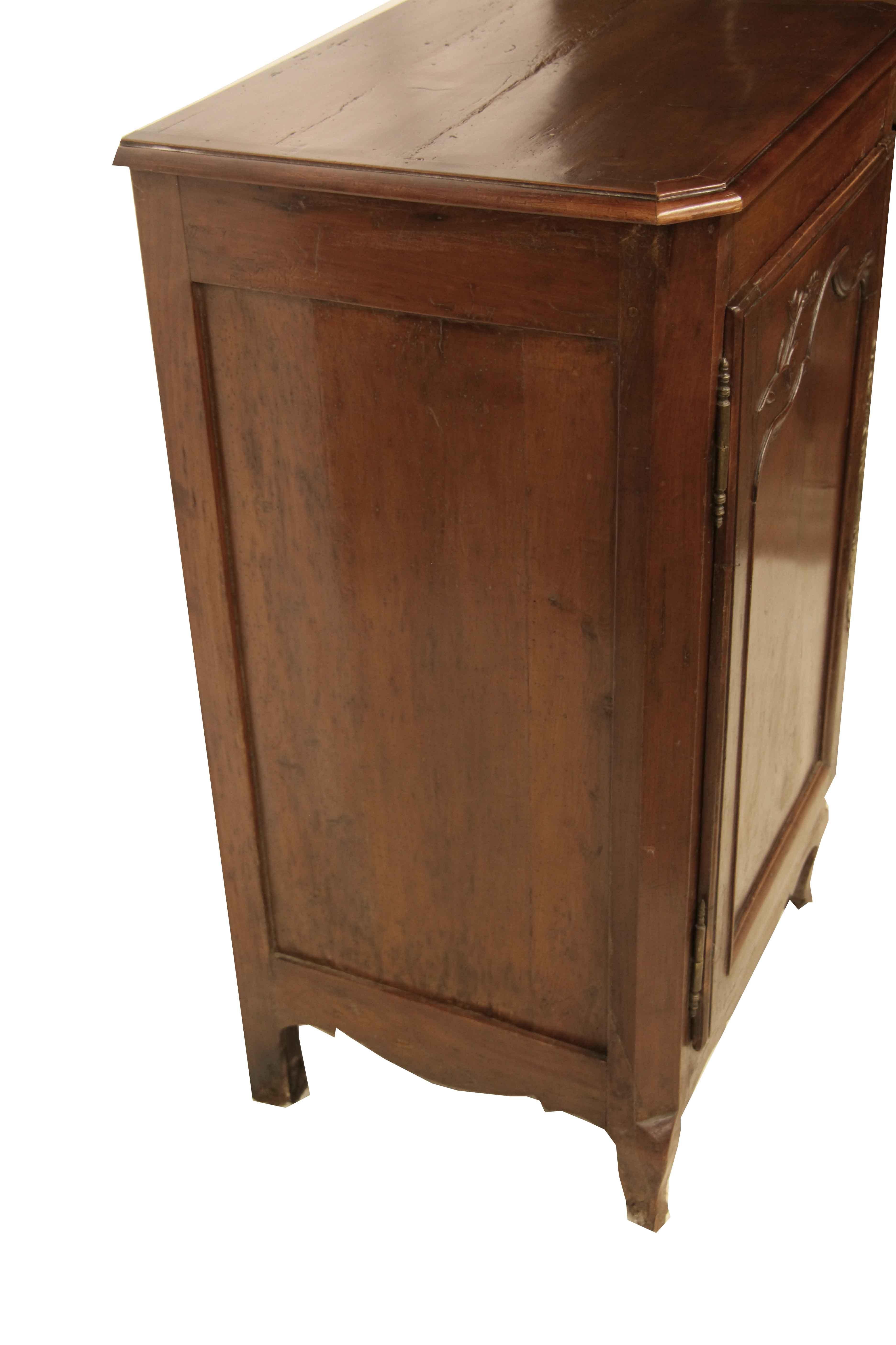 French cherry cabinet, the top with ''bread boarded'' and shaped edge molding , door and sides with inset panels, the door has carved foliate in relief and is hung on brass pin hinges, the long etched brass escutcheon is typical for the piece but is