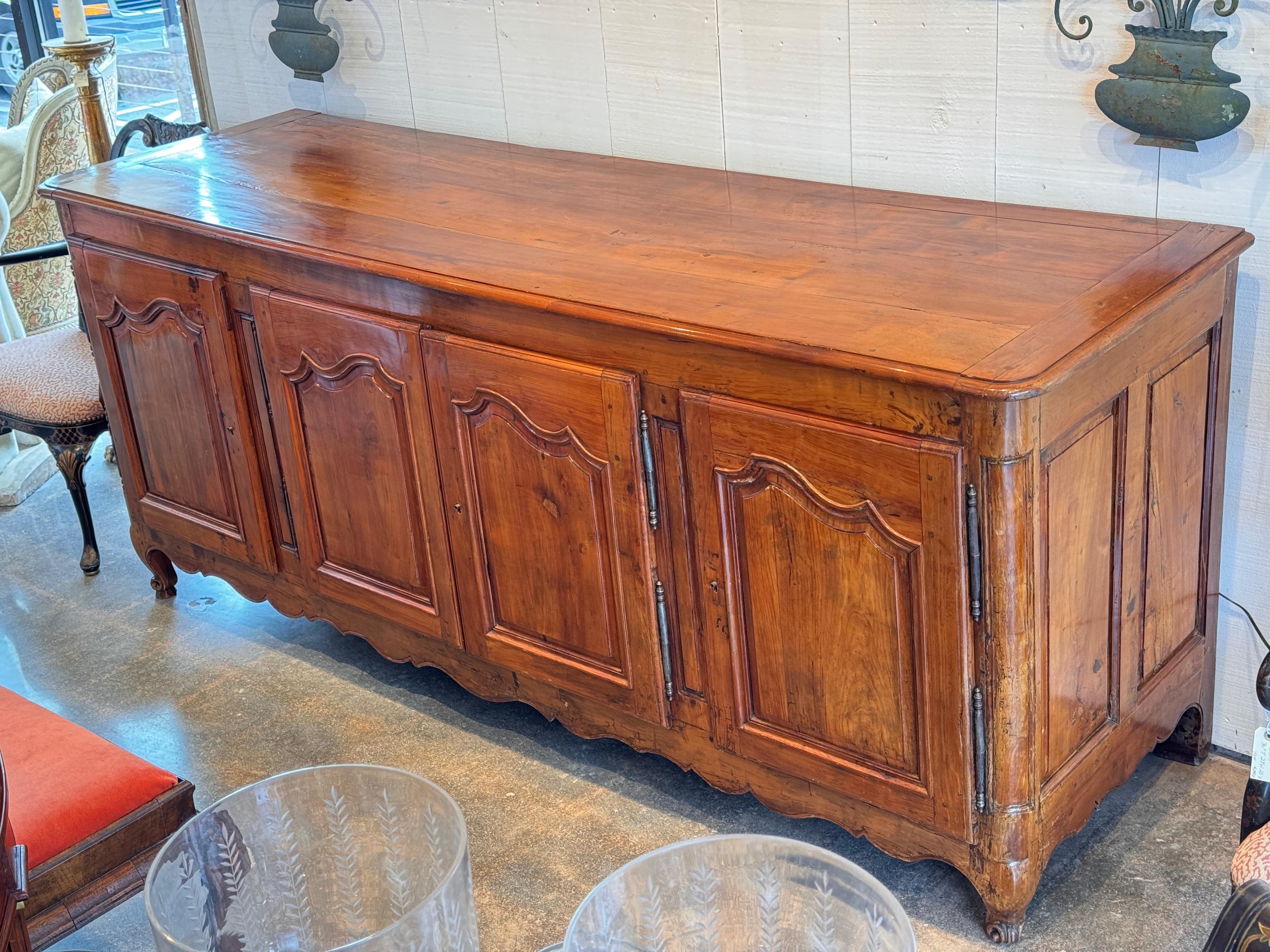 Eine massive französische Enfilade aus Kirschbaumholz mit vier getäfelten Türen mit Formleisten und traditionellen Wappenschildern. Der Schrank steht auf kurzen, geschwungenen Füßen und weist eine warme Patina mit natürlichen, altersgemäßen