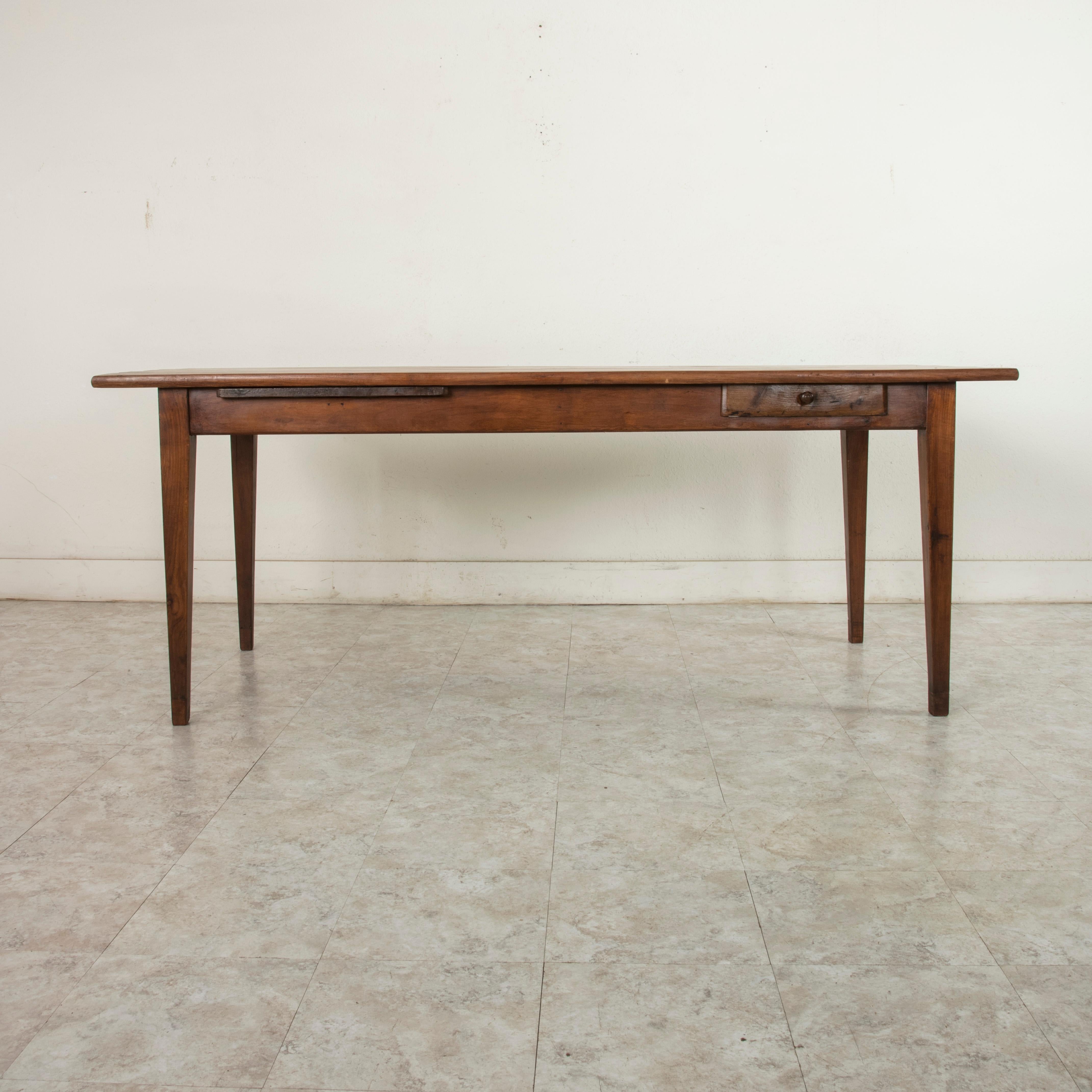 This artisan made farm table from the turn of the 20th century is from the region of Le Perche, a Sub-region of Normandy, France. Its cherrywood top measures 78.5 inches long and 32 inches wide. Resting on a cherrywood base of mortise and tenon