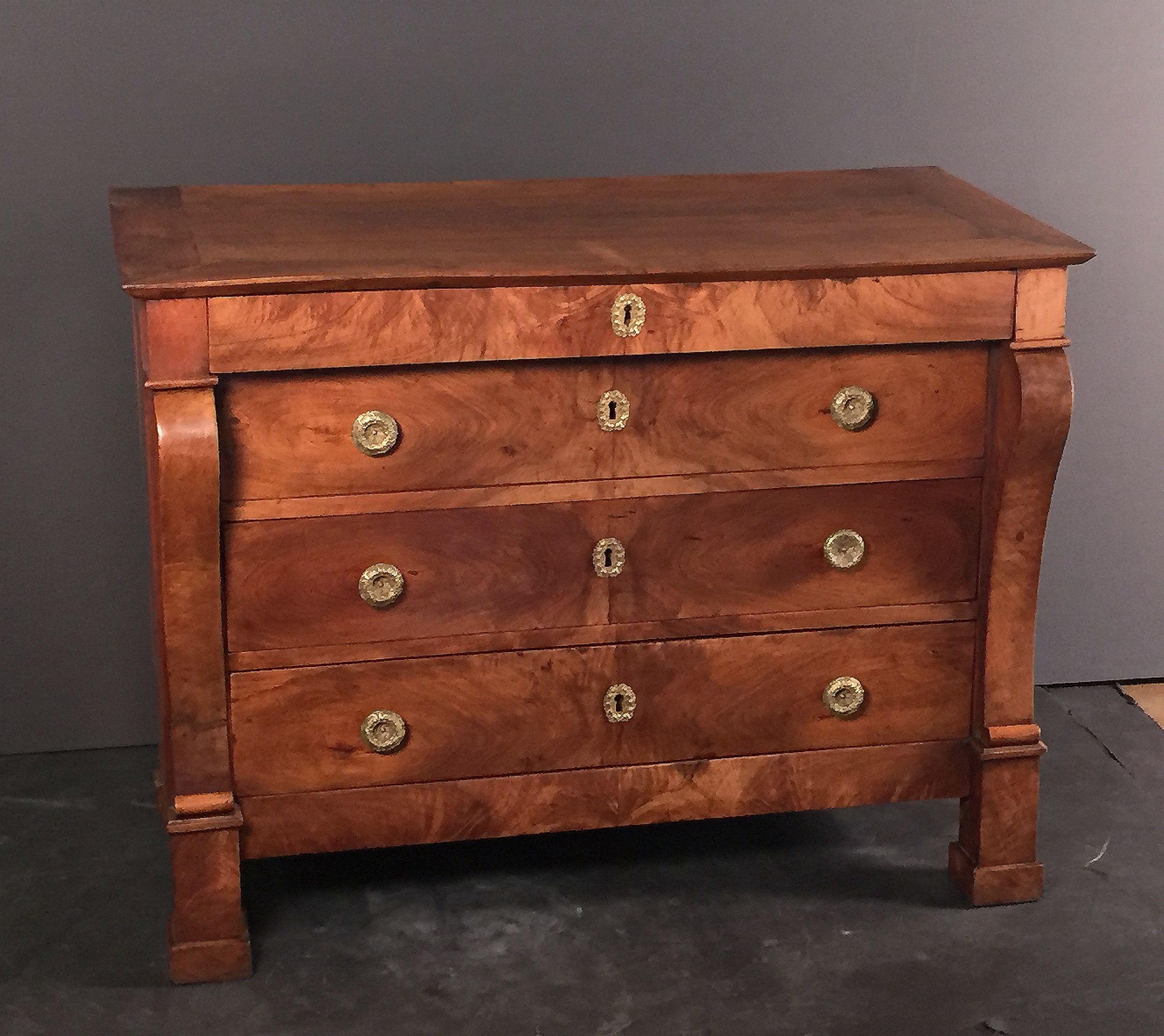A fine French chest of drawers of beautifully patinated walnut from the Restauration period, featuring four drawers with ornamental hardware and escutcheons, flanked on each side by curved consoles, and resting on shaped feet.