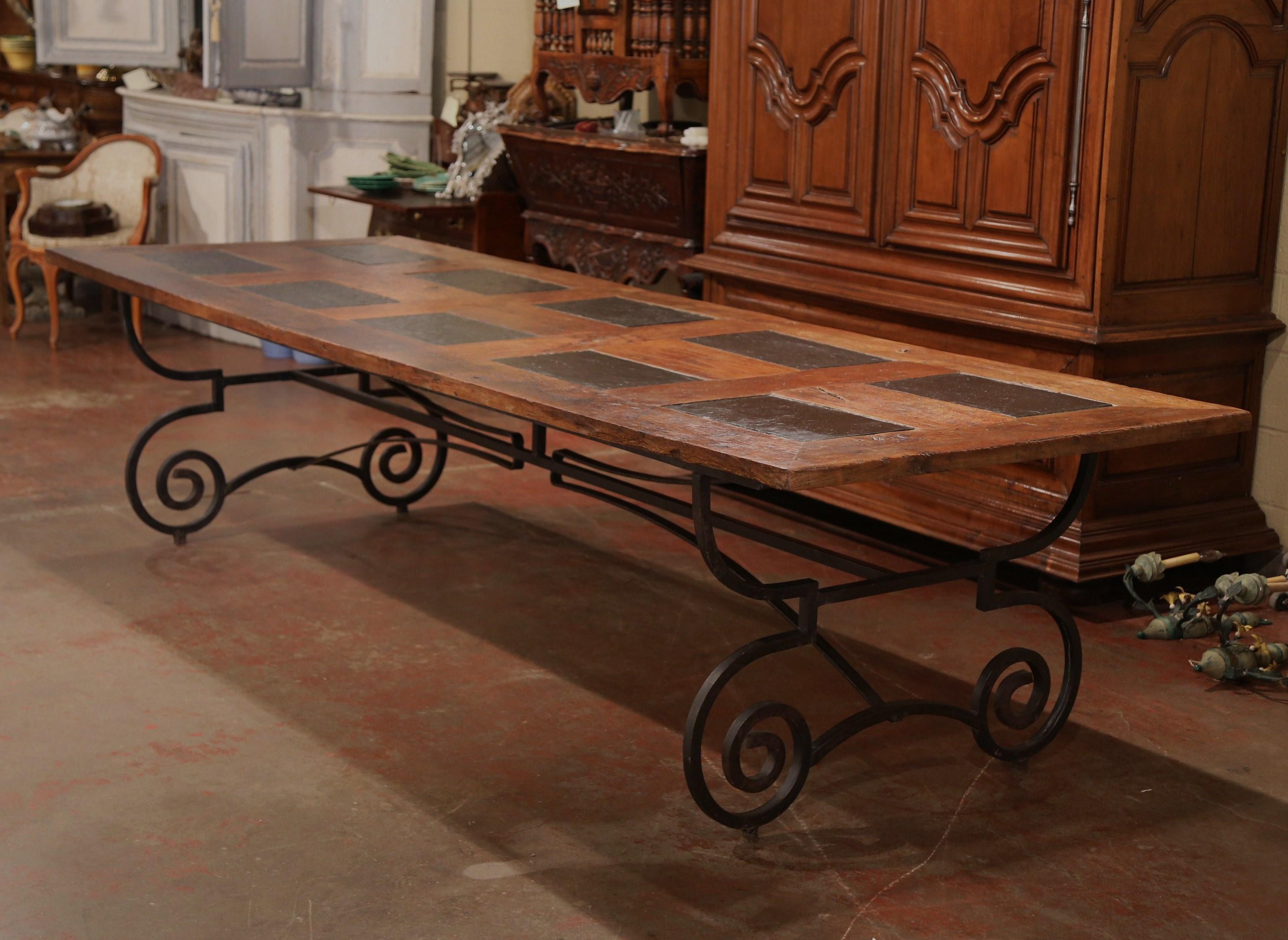 This large and long, antique dining room table was crafted in the French Pyrenees. The top plank is made from 18th century chestnut wood, and is decorated with eight large slate tiles on the surface for a symmetrical, geometric effect. The wide