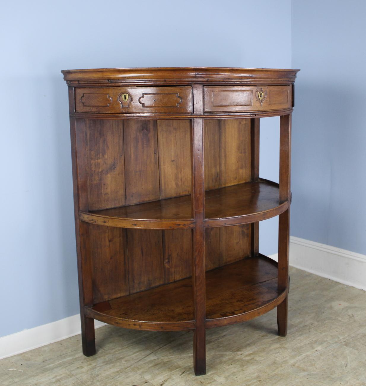 A large dramatic bookcase or server in glowing chestnut. Three drawers fit beautifully into the demi lune top, though are not on runners. Original brass hardware and two spacious shelves below, each 17 inches high. Unique!