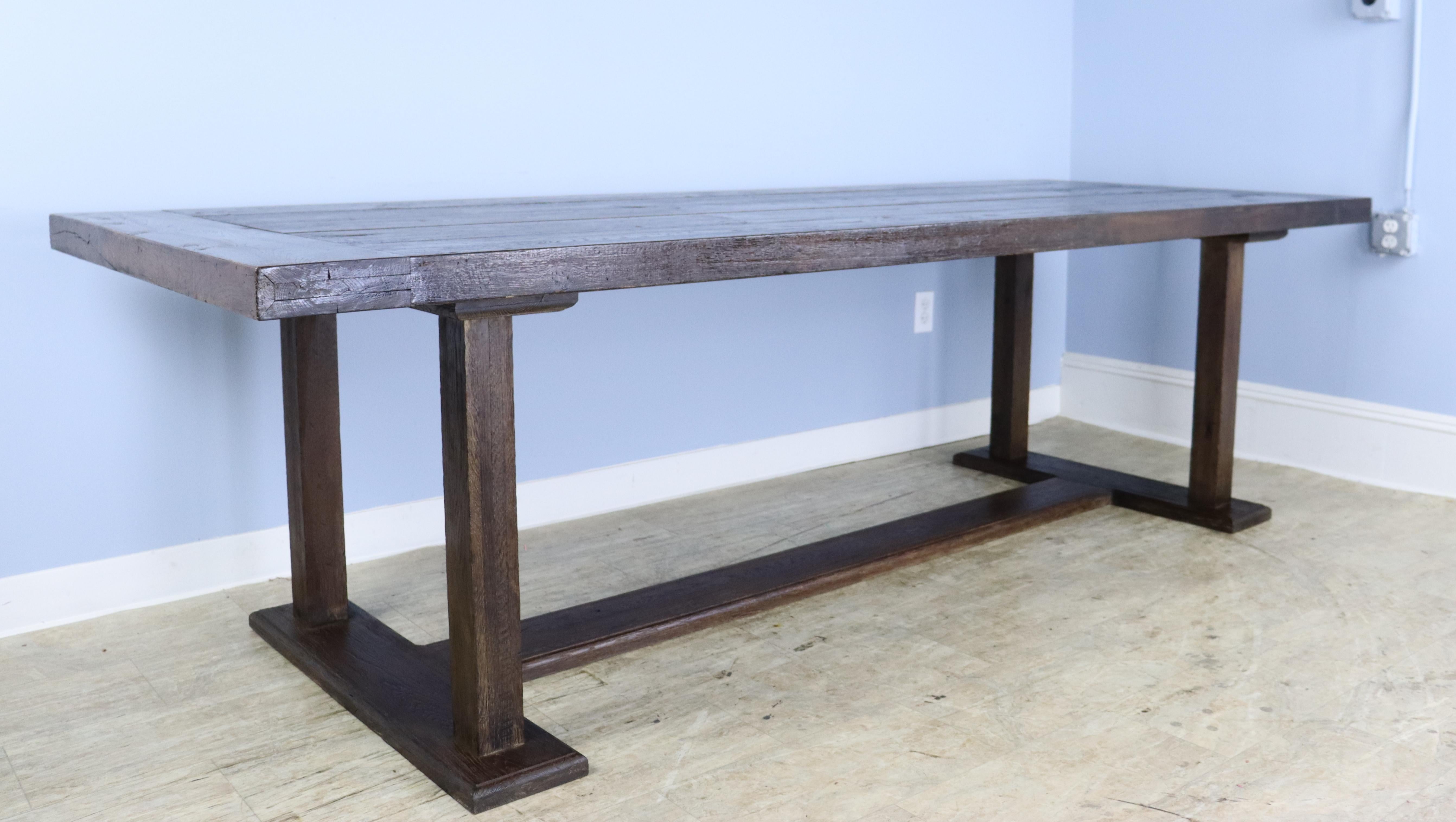 A generously proportioned long dark farm table with a stretcher base and a patinated topwith breadboard ends. The top has good chestnut texture, and the trestled legs at the base add a note of grandeur. Great depth. The apron height is good for