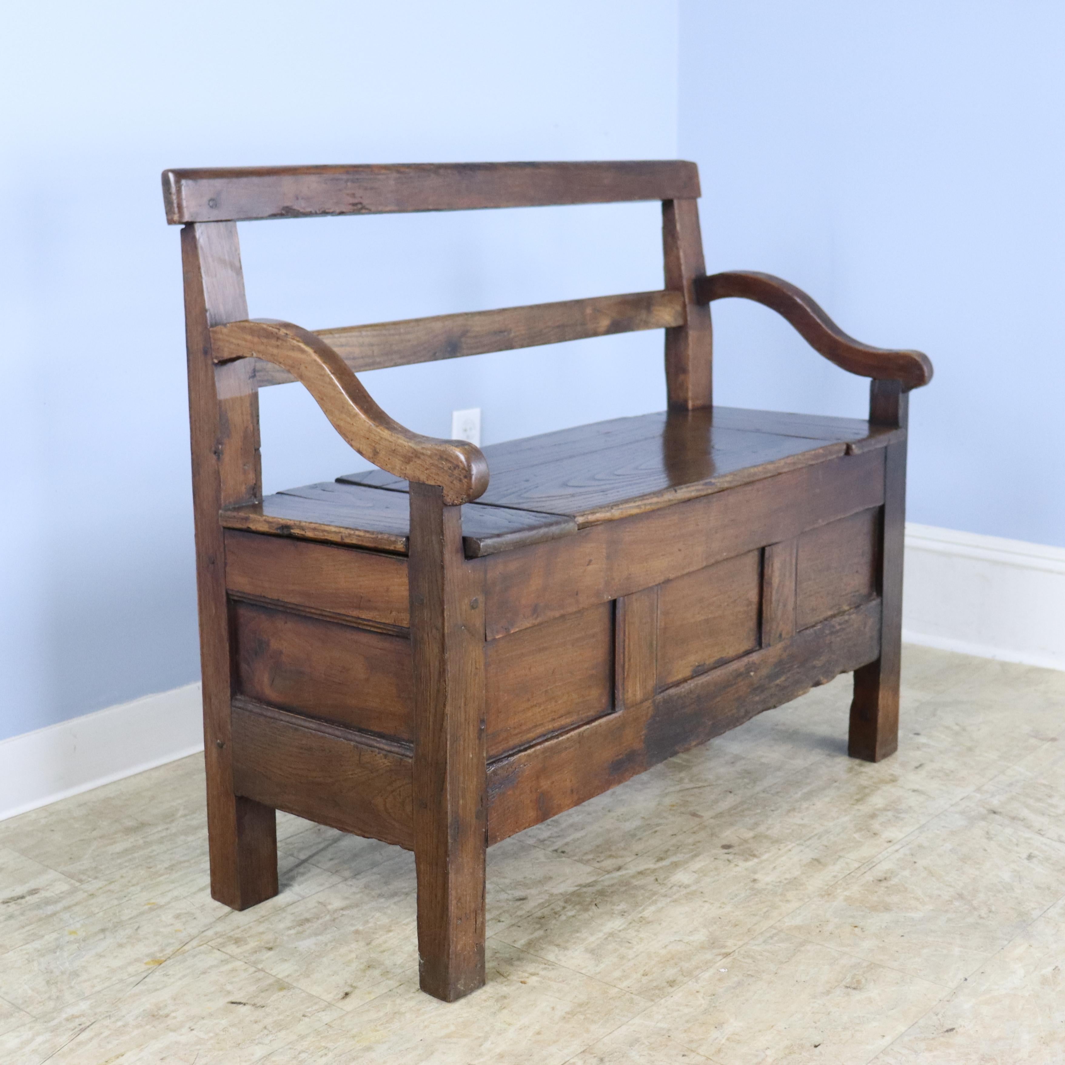 A handsome chunky chestnut bench with lots of good wear and a lift up seat with good storage.  Graceful curved arms. The interior of the storage compartment is quite clean.  There is some wear on the front of the piece, shown in thumbnails.