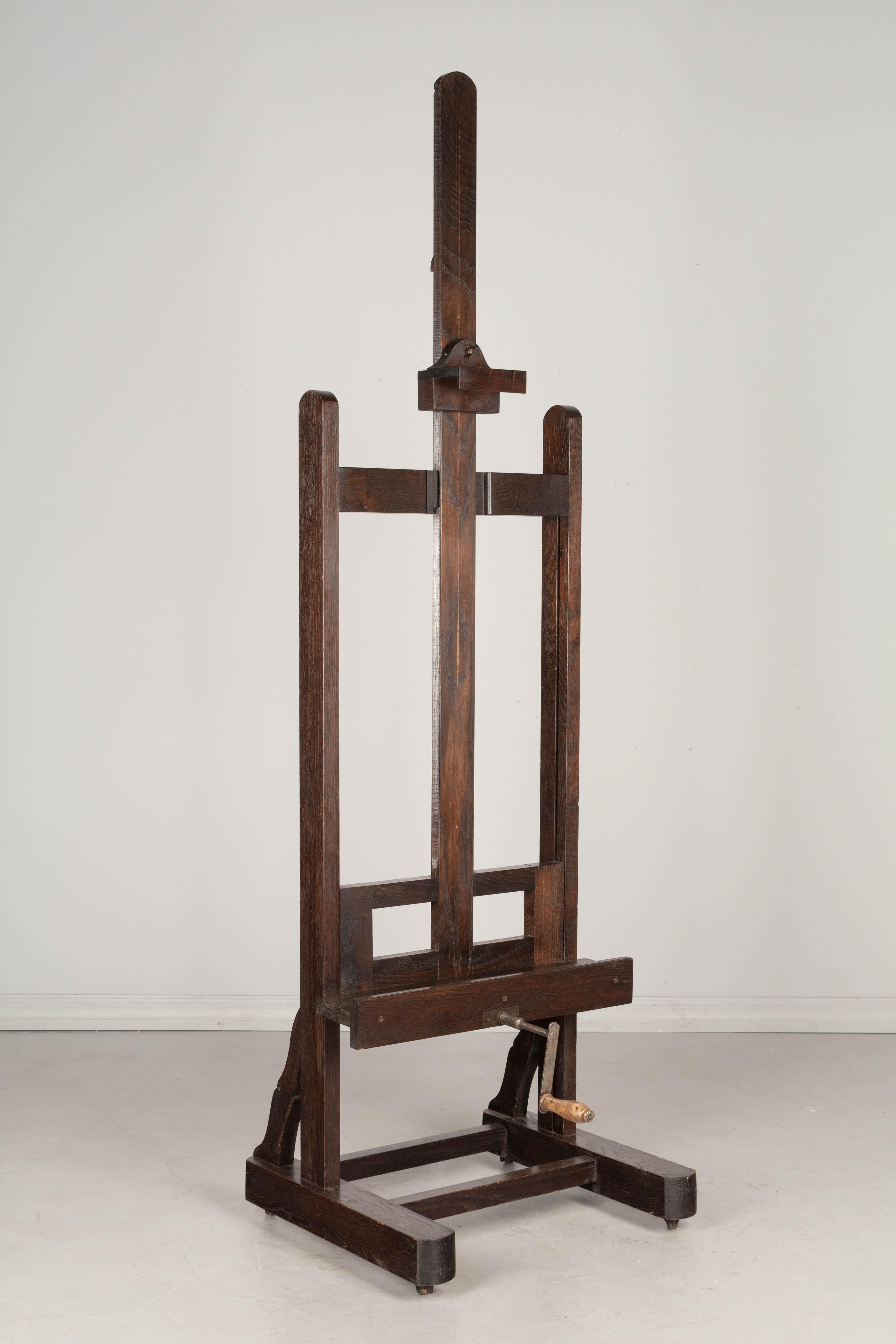 A French painter's easel made of solid oak with threaded rod, cast iron gear and turned wood handled crank. A deep ledge and a new adjustable bracket at the top securely holds the painting in place. Very sturdy base with original castors. Small