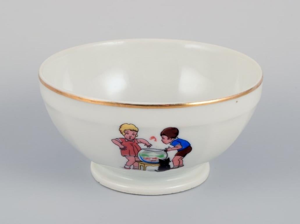 French children's porcelain dinnerware consisting of a bowl, egg cup, pepper shaker, miniature sauce boat, and a small oval dish. 
Motifs of children at play.
From the 1930s/1940s.
In very good condition with signs of use.
Bowl: 11.5 cm in diameter