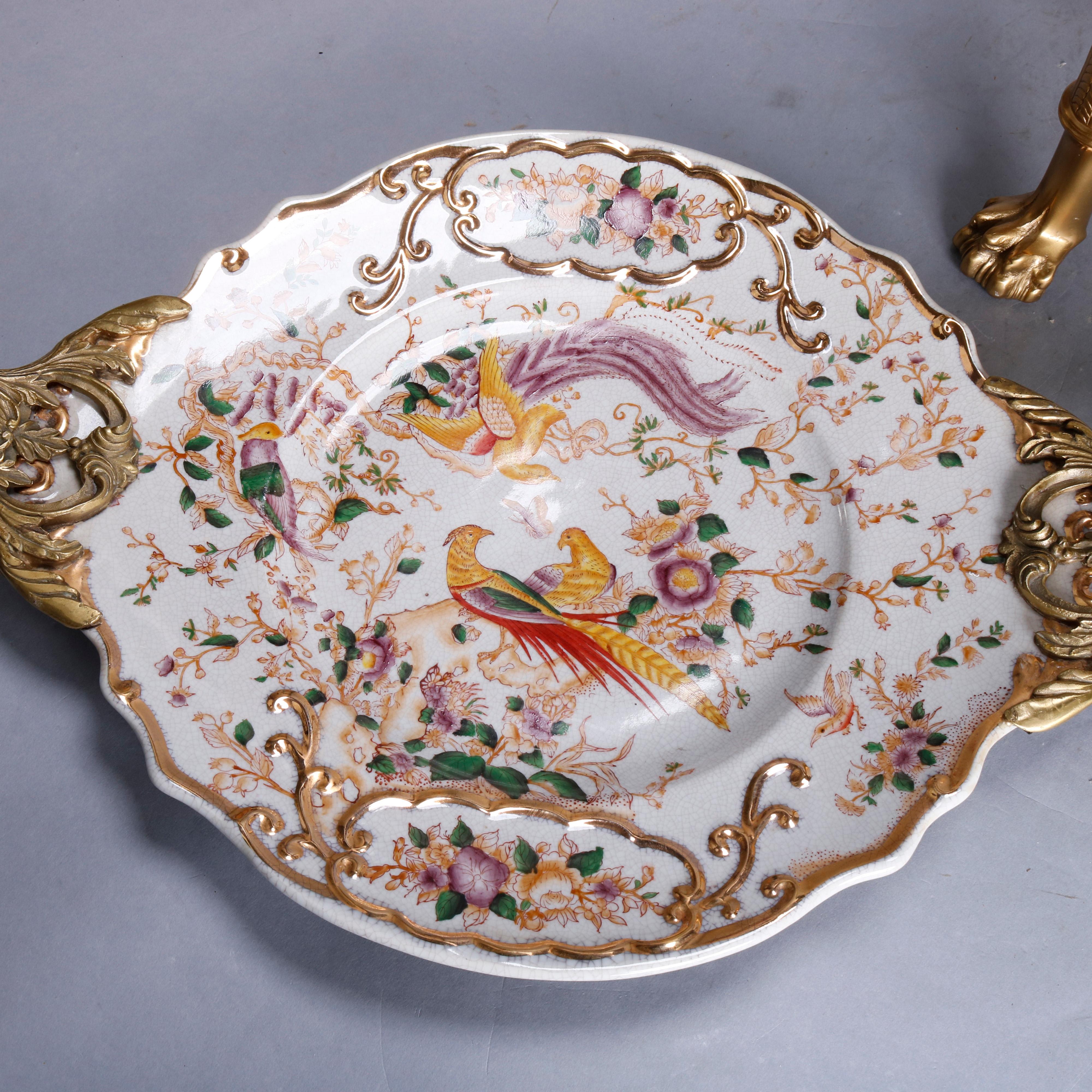 A French Chinese Chippendale plaque side table offers a double handled chinoiserie hand painted and gilt porcelain tray depicting pheasants in garden setting and surmounting a gilt bronze base having double falcon figural handles and braided apron