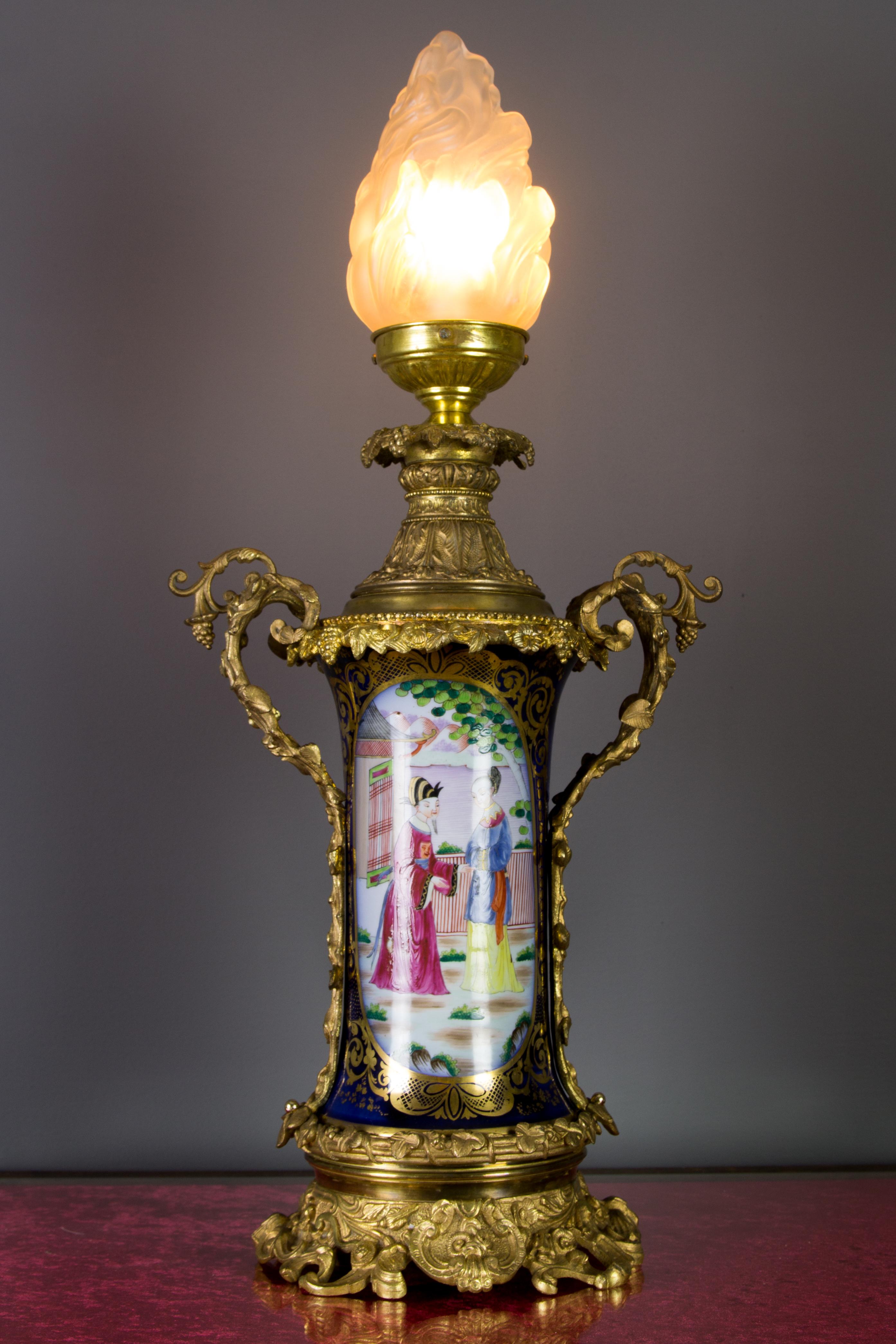 This amazing and large late 19th-century oil lamp mounted on a gilt bronze base and fitted with bronze cap and handles, features a cobalt blue and hand-painted porcelain body with Chinoiserie style colorful scenes. Ornate gilt bronze details in
