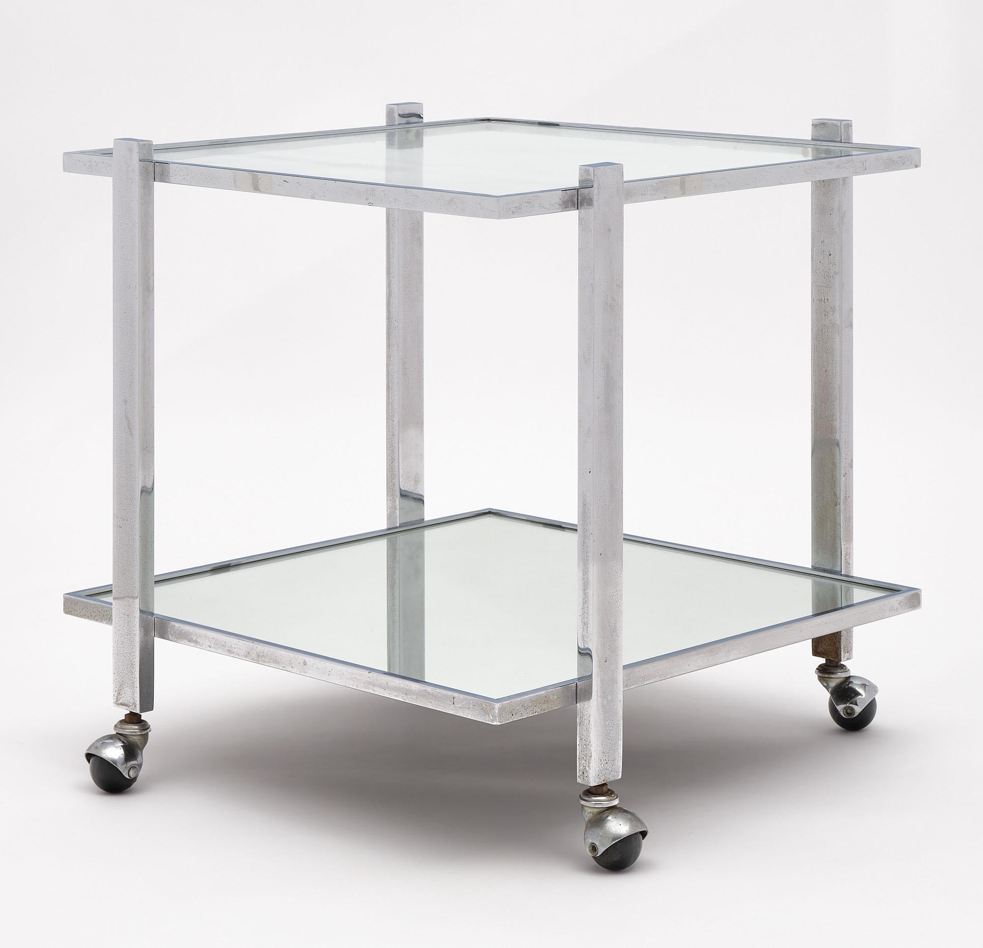 Side table from France made of chromed steel with a square sectioned structure with clear glass top shelf and mirrored bottom shelf. This piece is supported by casters. We love the modernist lines of this piece.