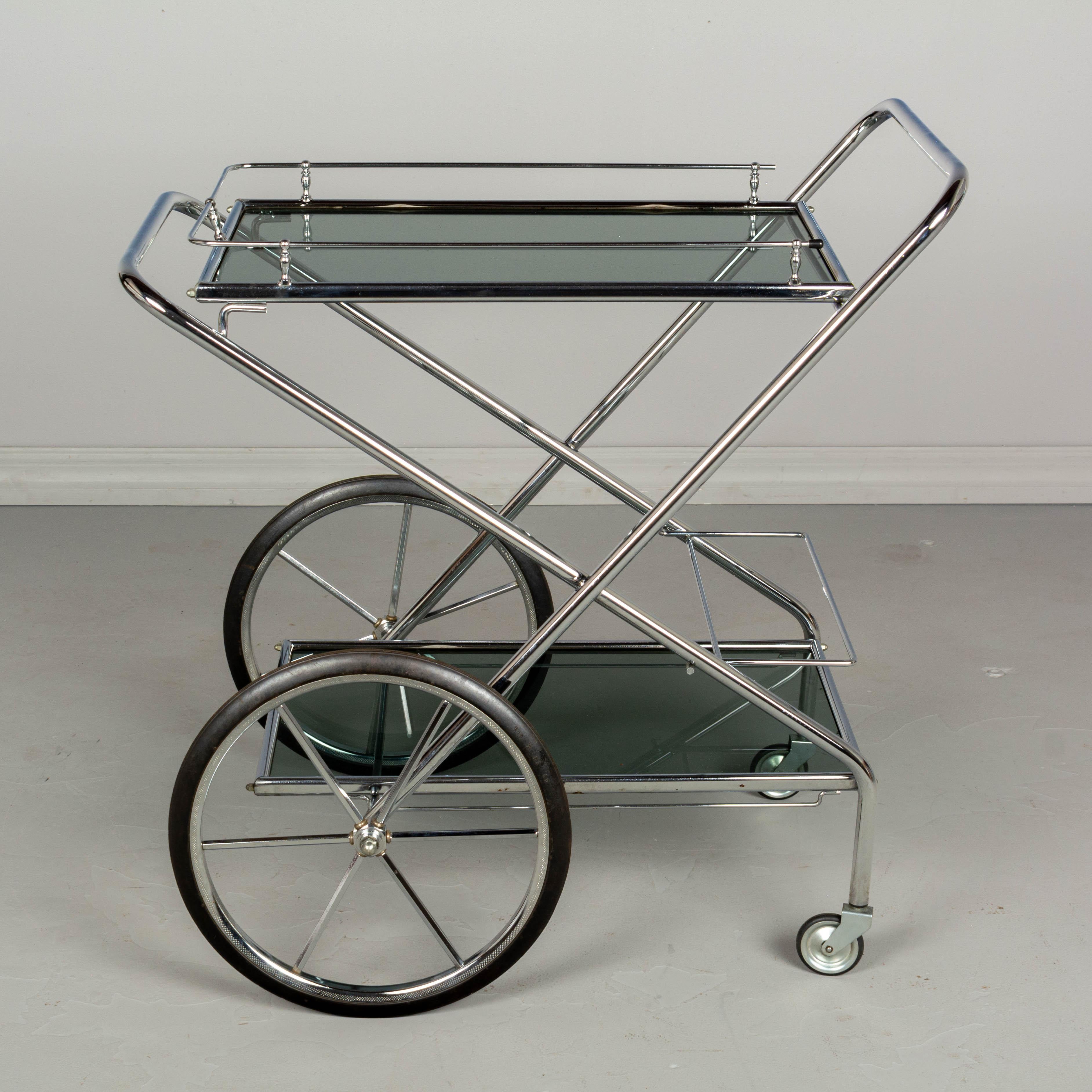 A French folding bar cart, or drinks trolley, made of tubular polished chrome with smoke glass shelves. The X-shaped frame is hinged and can be folded for easy storage. Superb design and well-made. Original rubber wheels glide smoothly. 26