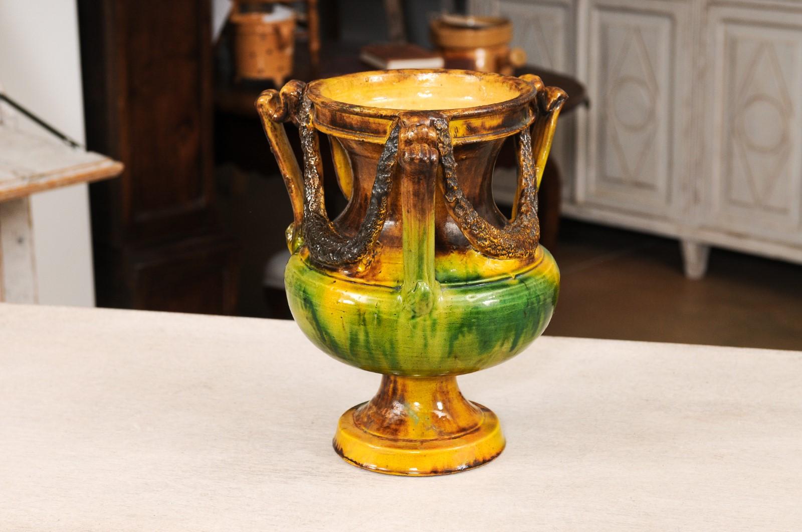 A French Anduze vase from the 19th century with brown, green and yellow glaze, molded handles and swag motifs. Enhance your outdoor space with this stunning French Anduze vase from the 19th century. Adorned with a beautiful combination of brown,