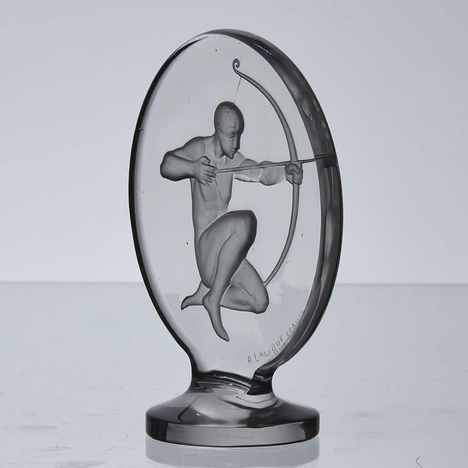 Exquisite French, early 20th century Art Deco clear glass car mascot in roundel form engraved with the figure of a kneeling Archer with intricate hand carved detail, raised on a circular plinth and signed R Lalique France

Archer
Catalogue