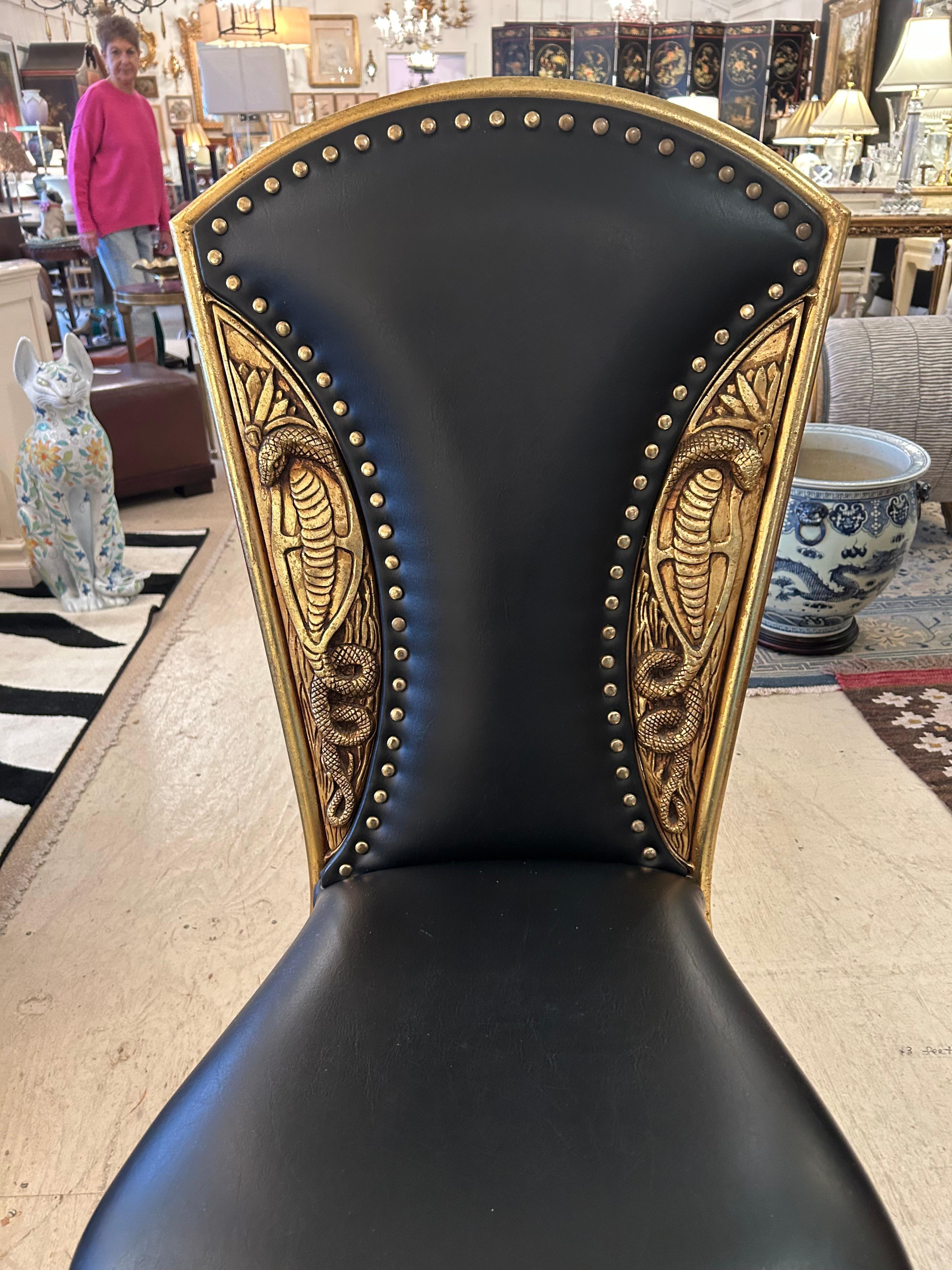 Una llamativa obra de arte en una silla auxiliar, con relieves de latón o metal dorado con serpientes cobra en los laterales y el respaldo, con atractivas cabezas de clavos de latón sobre tapicería de cuero negro.  Elegantes patas finas de metal.