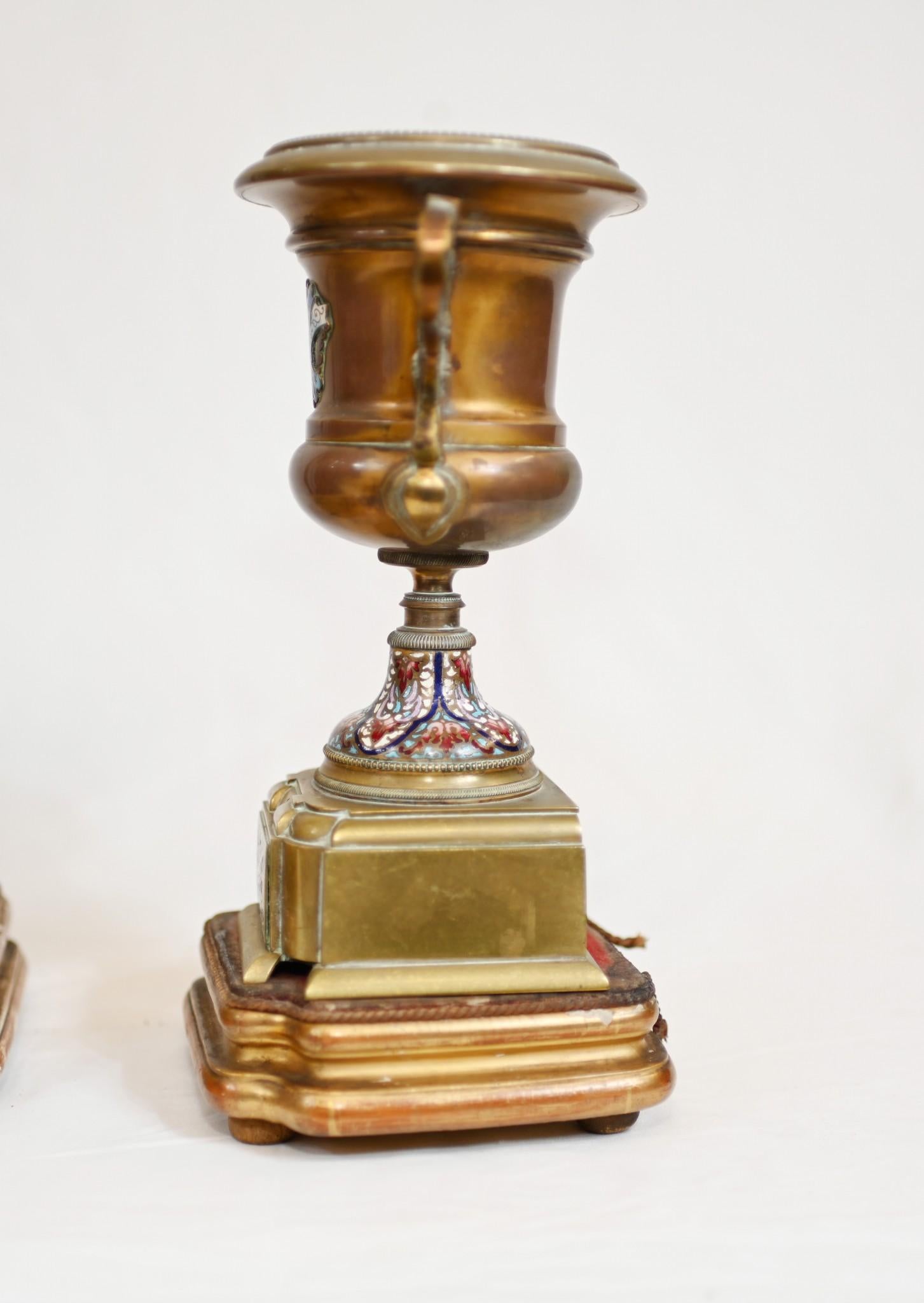 Gorgeous antique French three piece clock set
Mantle clock is flanked by the two urns 
We date this to circa 1860
Set features intricate champleve designs on all surfaces
Champleve is a decorative technique that fuses a powdered glassy Material