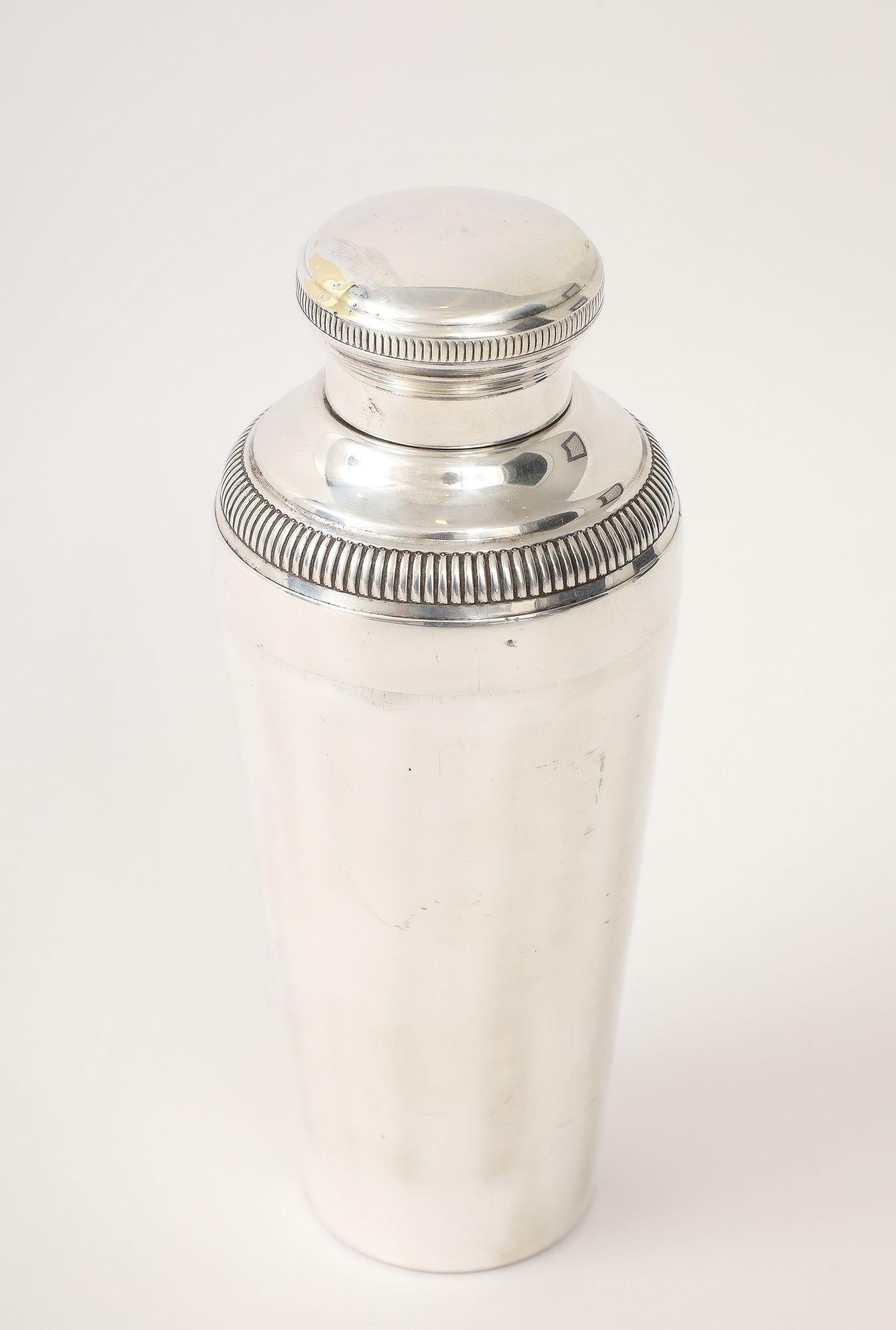 An authentic French Art Deco silver-plated cocktail shaker from the 1930s. Its sleek, tapered design and distinctive reeded band embody the sophisticated glamour of the era. This functional and decorative piece retains a beautiful luster with