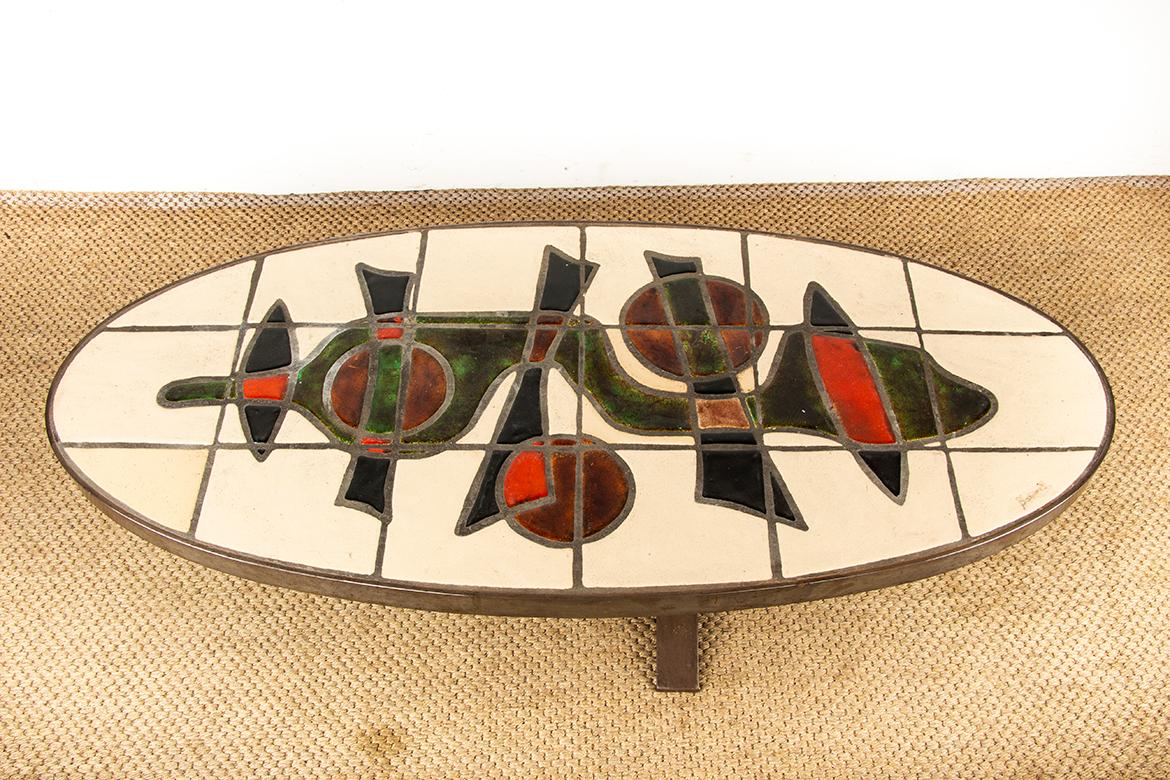 Splendido tavolino da caffè Vallauris AM caratterizzato da una splendida ceramica con motivi moderni e una forma ovale. Elegante e originale base in metallo a forma di arpa. Un mobile raffinato, degno delle migliori creazioni di Roger Capron, tipico